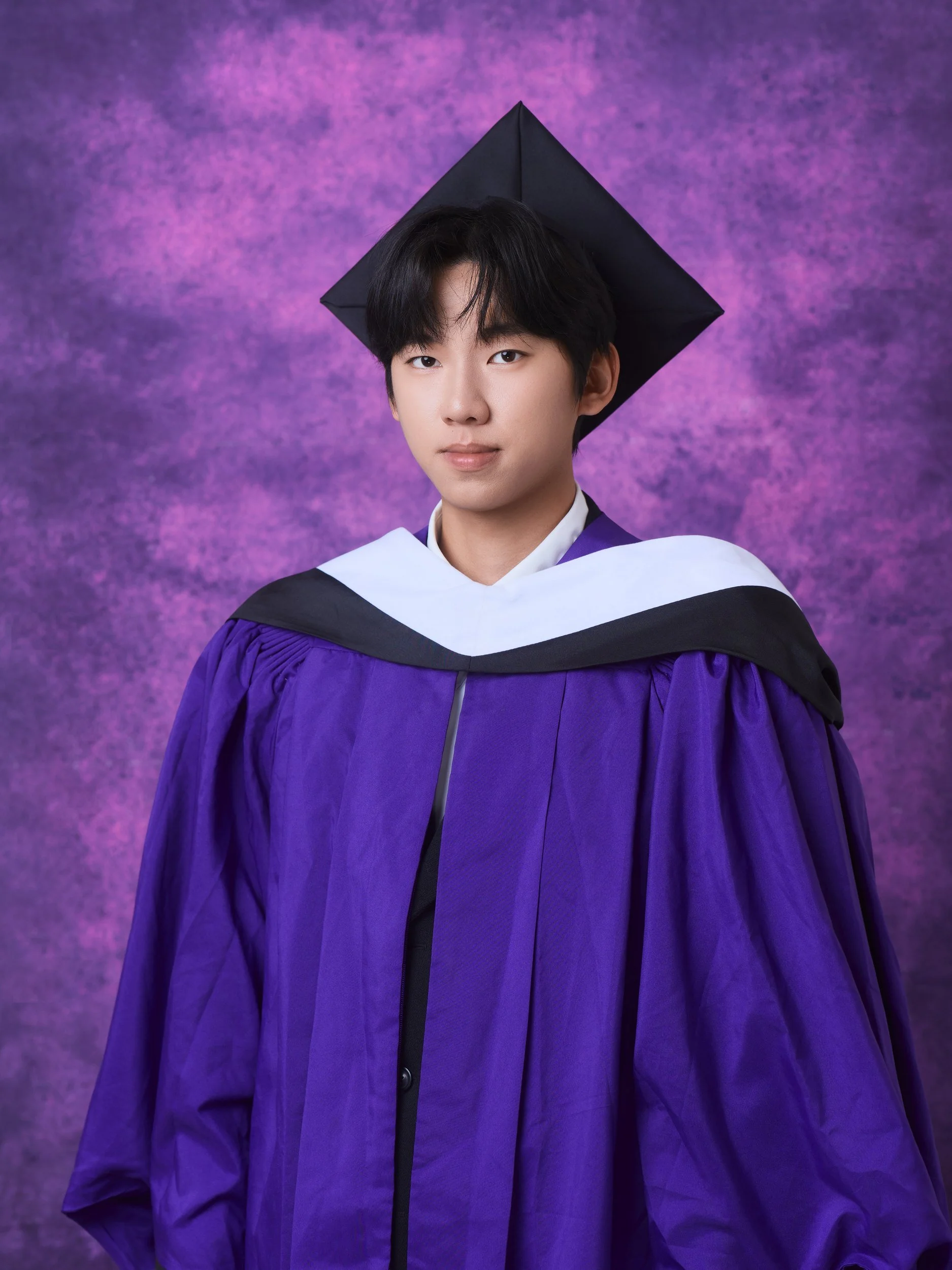 NYU graduation portrait of a young man with long hair in a purple gown and cap