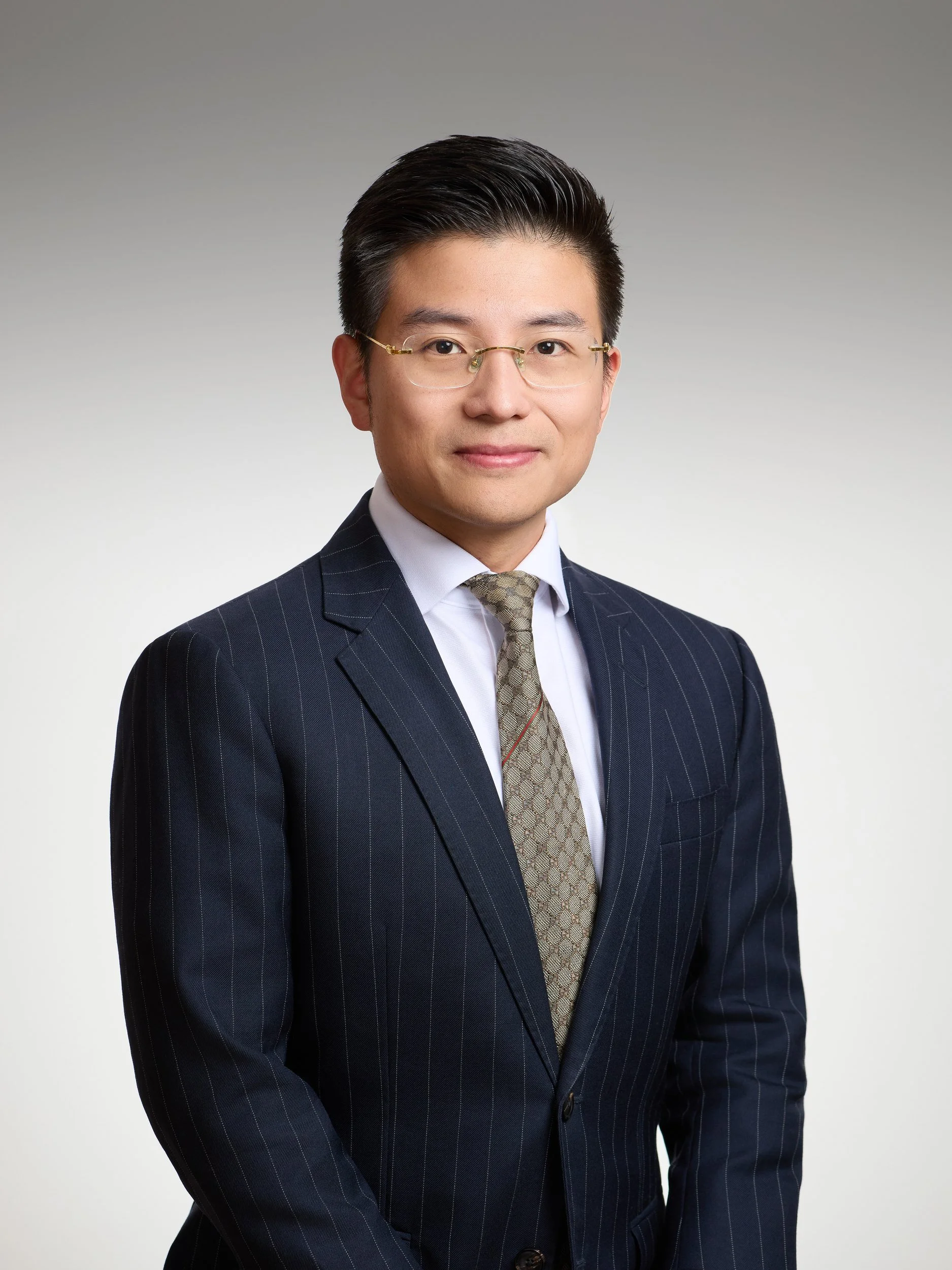 Corporate headshot of a man with glasses in a pinstripe suit on a grey gradient