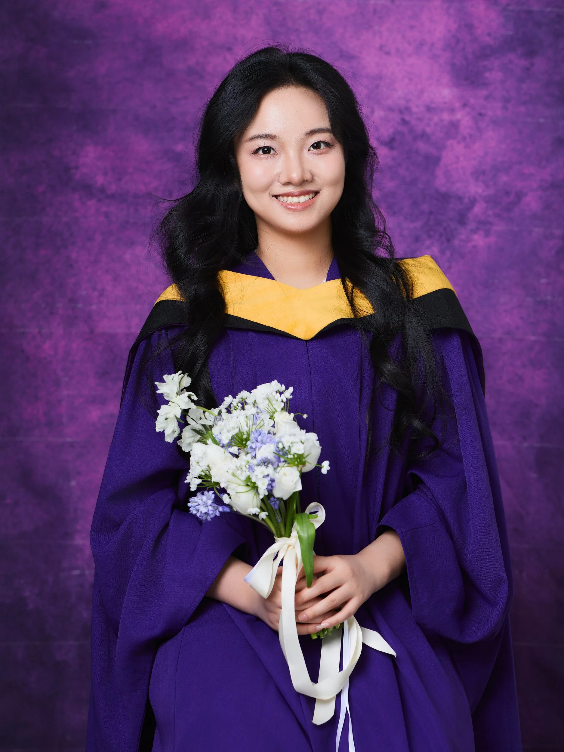 NYU graduation portrait of a smiling woman holding a bouquet of white flowers