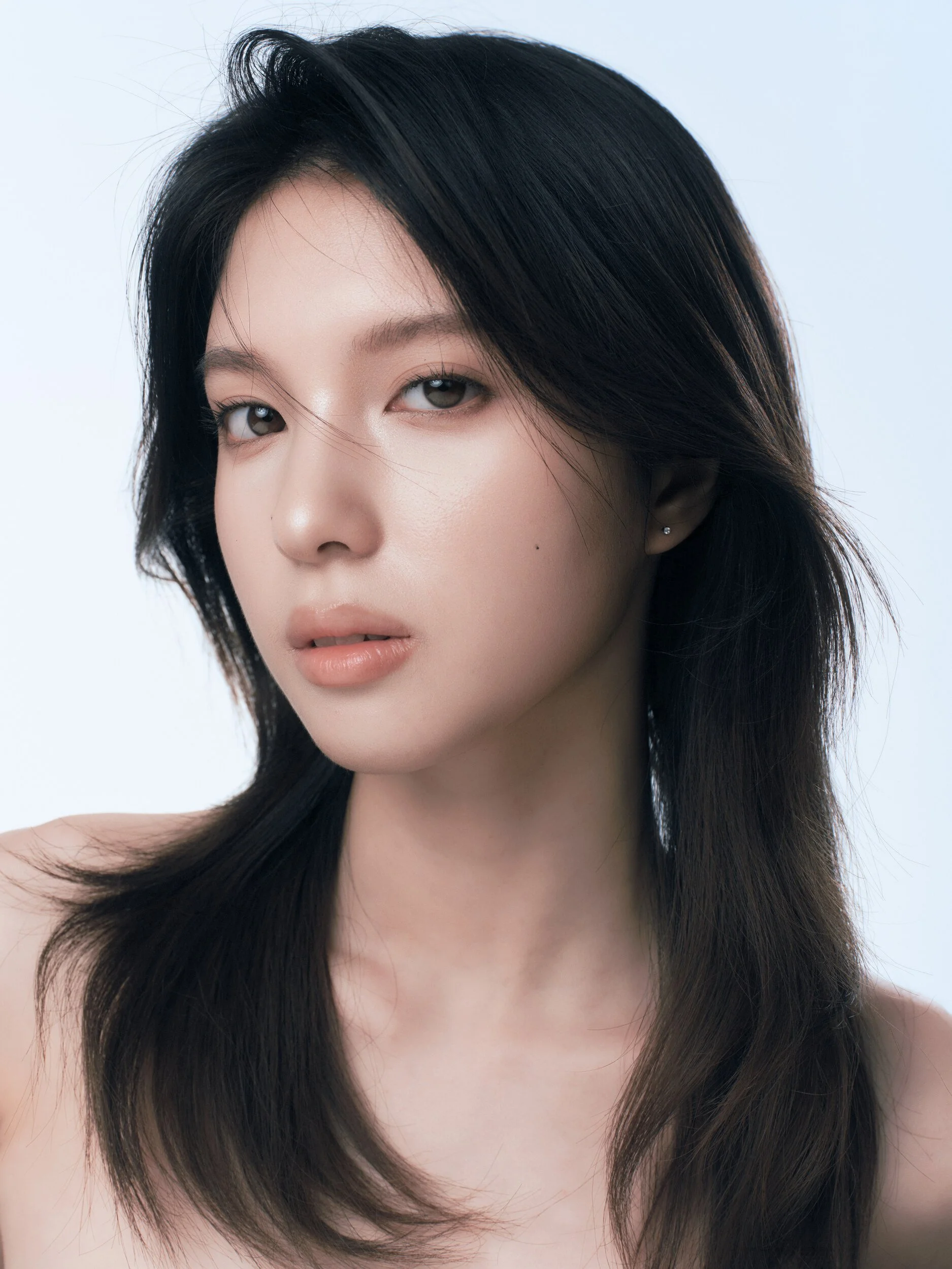 Clean beauty portrait of the same model looking into the camera, long layered hair and luminous skin on a pale blue backdrop