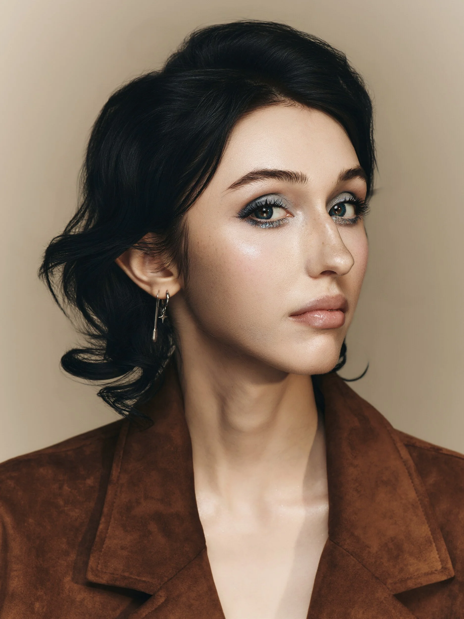 Three-quarter beauty portrait of the same model in a brown suede jacket on a warm beige backdrop