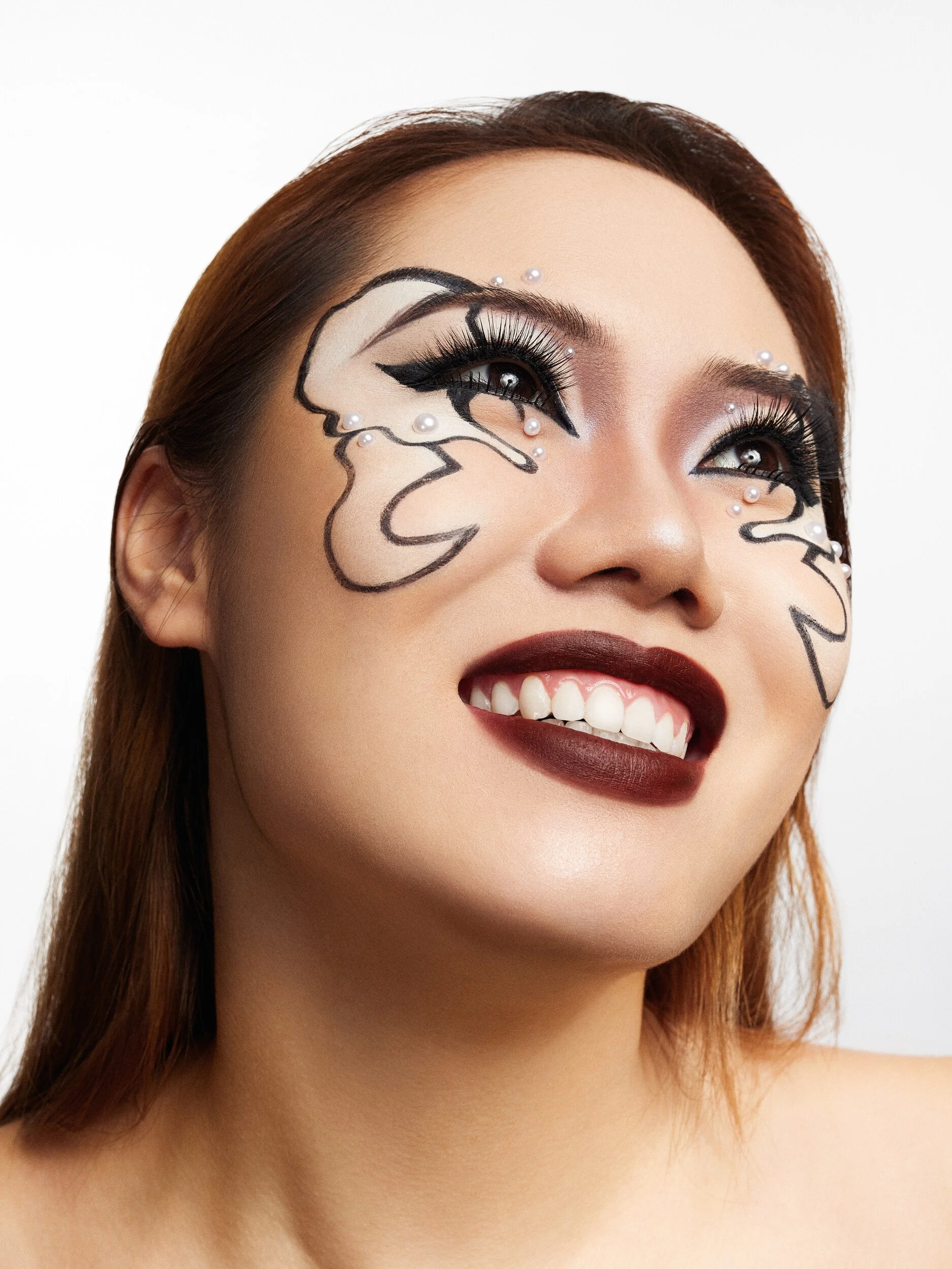 Smiling beauty portrait with graphic black liner swirls, pearl accents and burgundy lips, head tilted upward