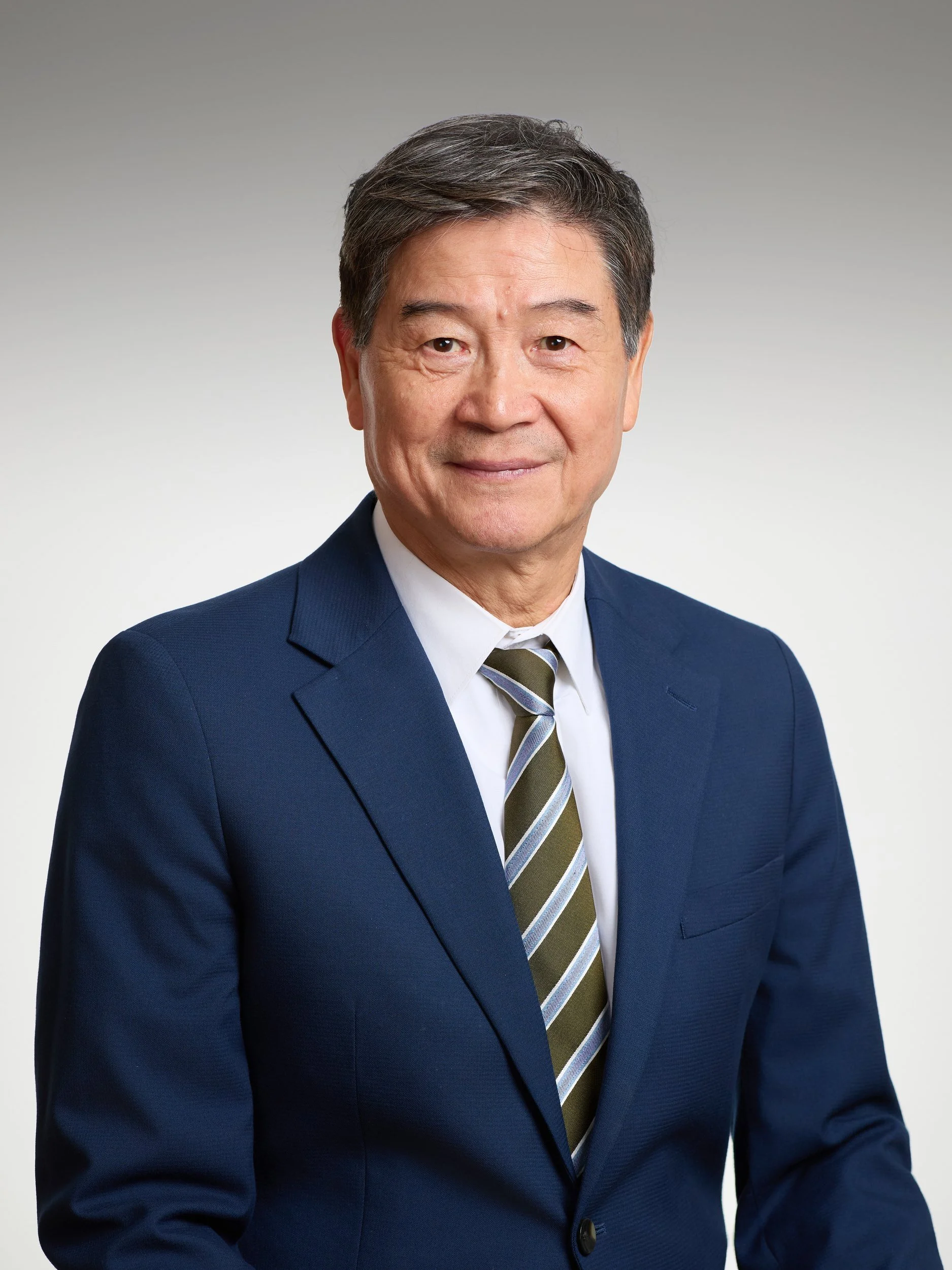 Corporate headshot of a man with grey hair in a navy suit on a grey gradient