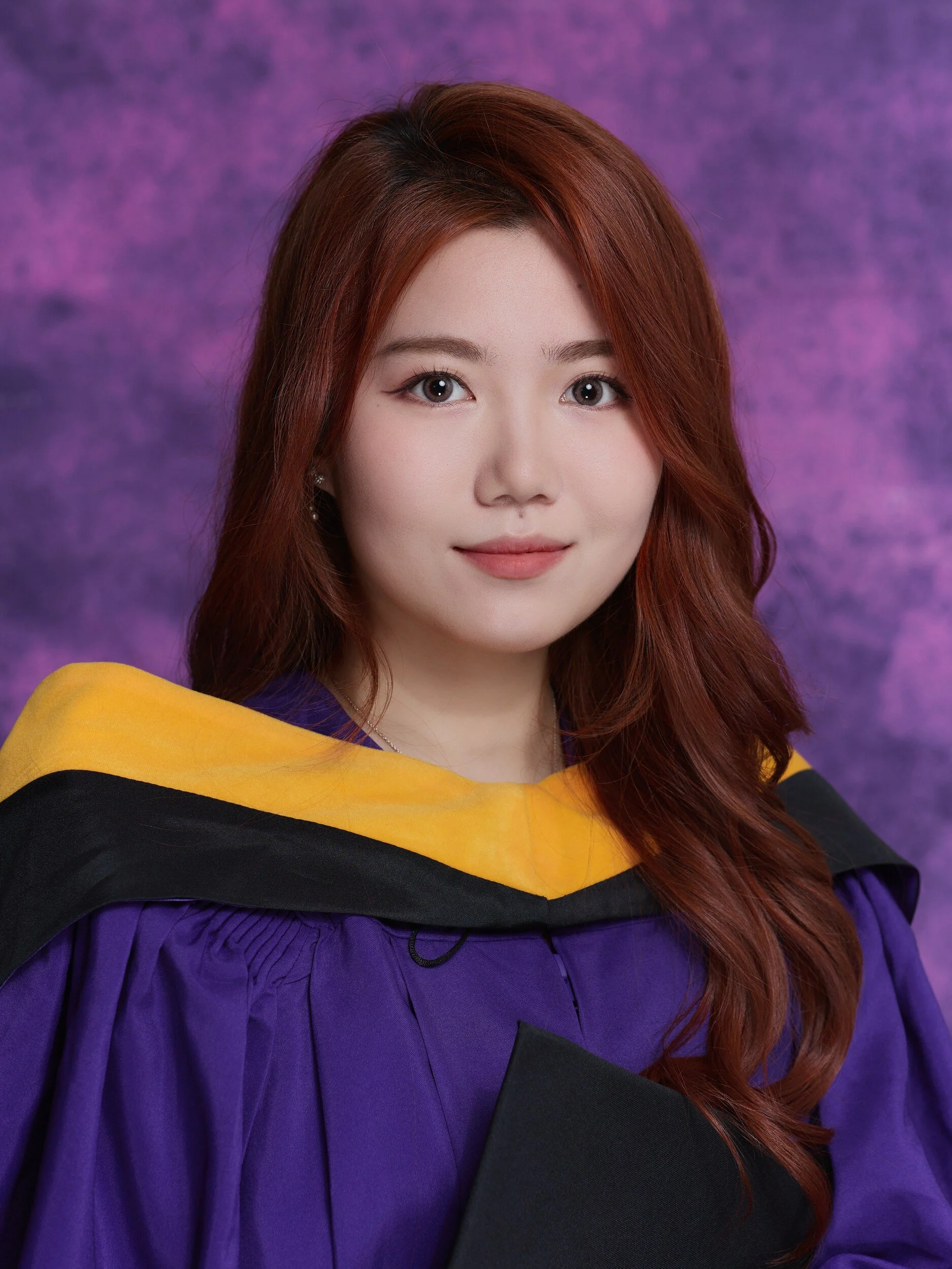 Close-up graduation portrait of a woman with auburn hair and a gold-trimmed hood