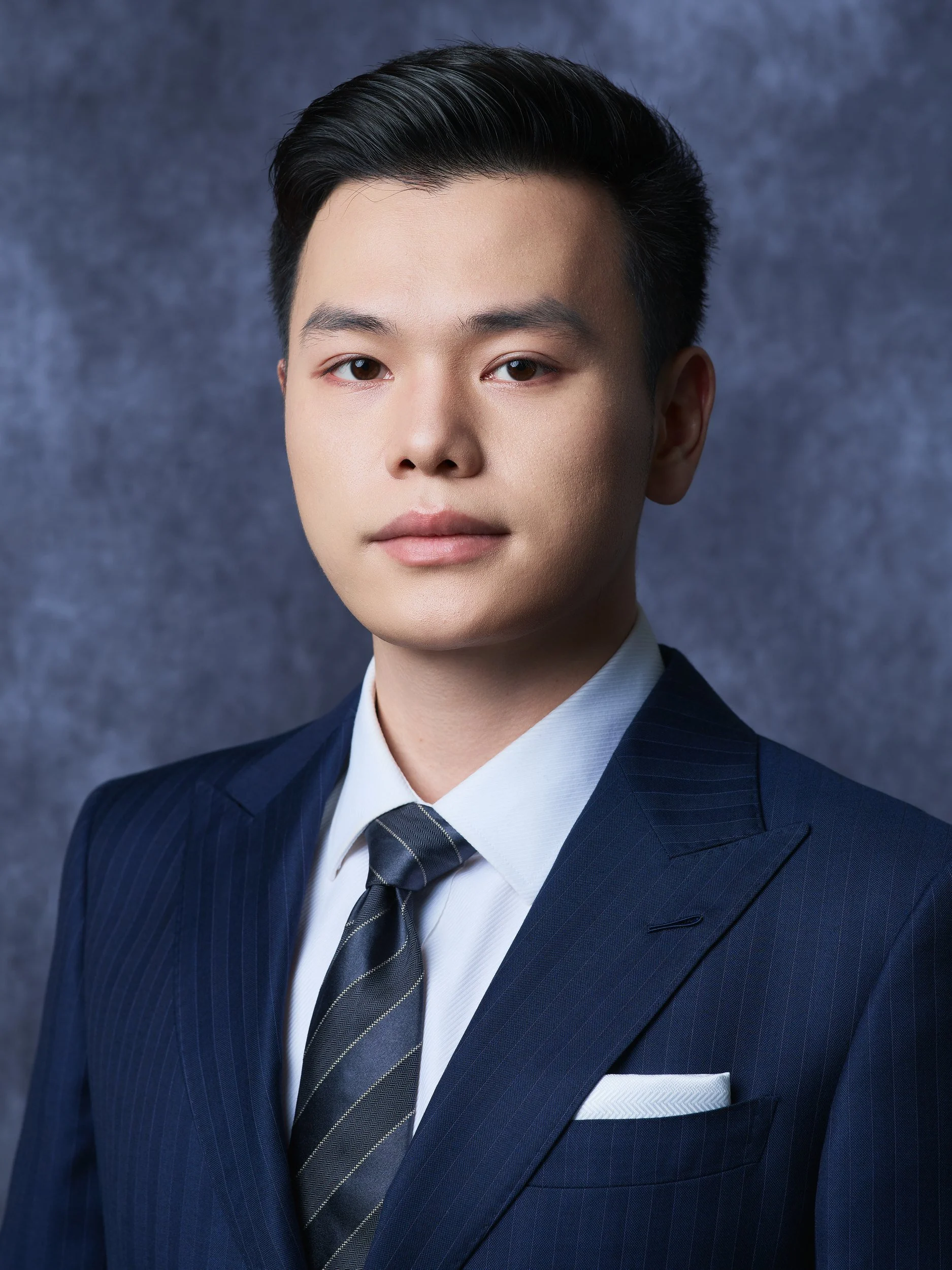 Professional headshot of a man in a navy suit and tie on a dark textured backdrop