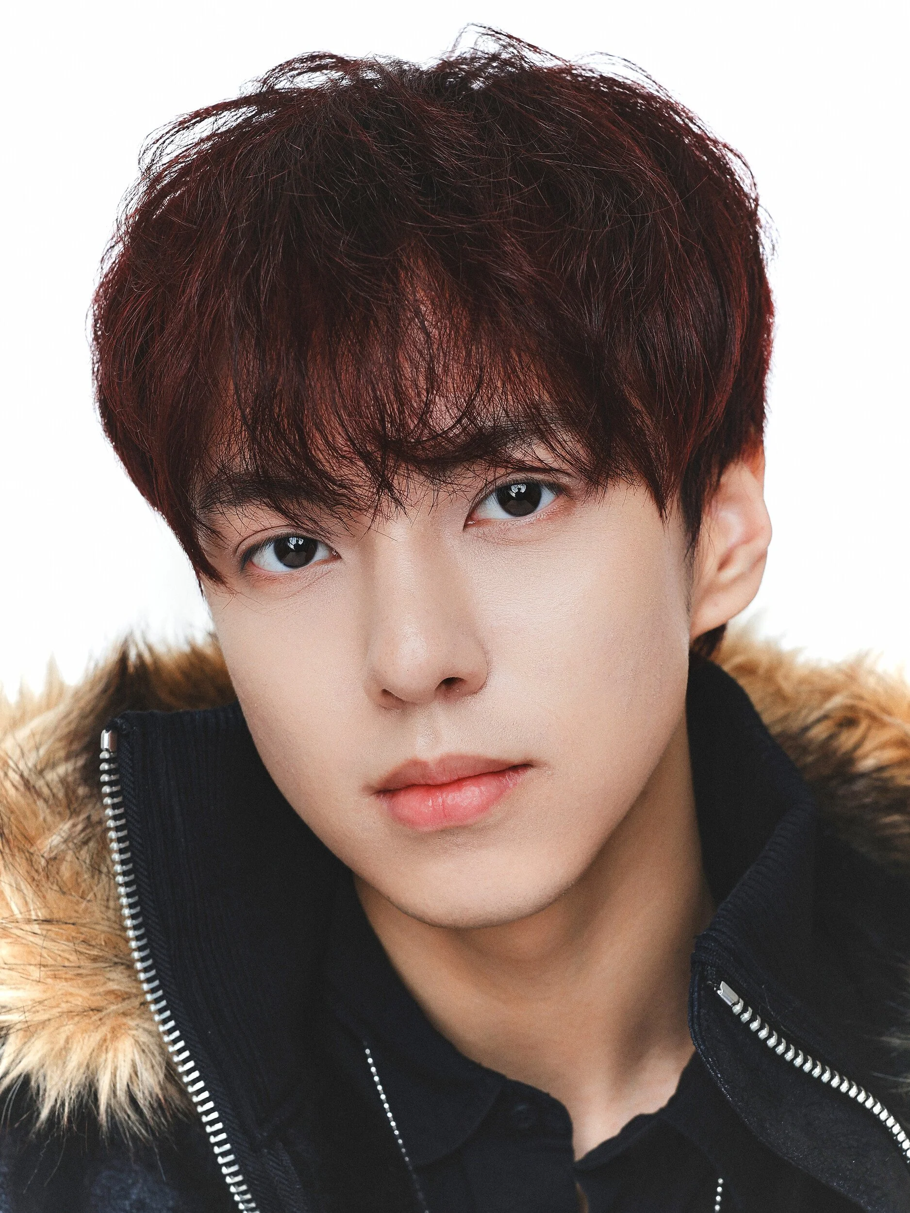 Close-up studio portrait of a man with dark red hair in a fur-hooded jacket