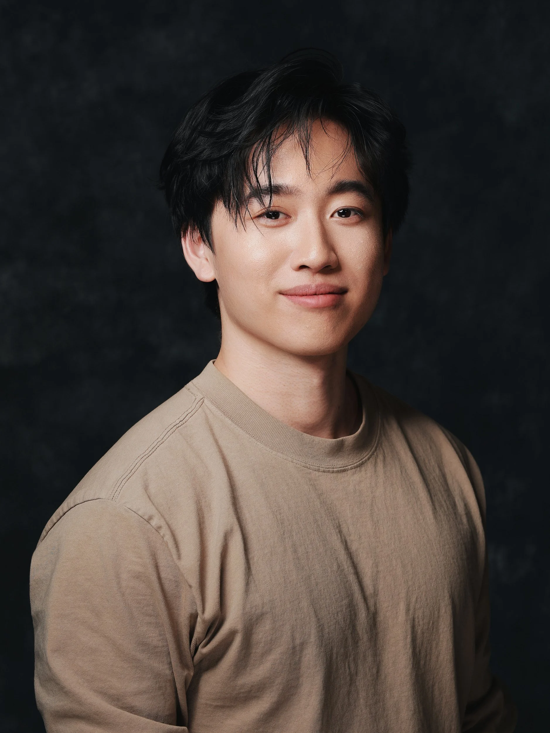 Portrait of a smiling man in a beige T-shirt on a dark backdrop