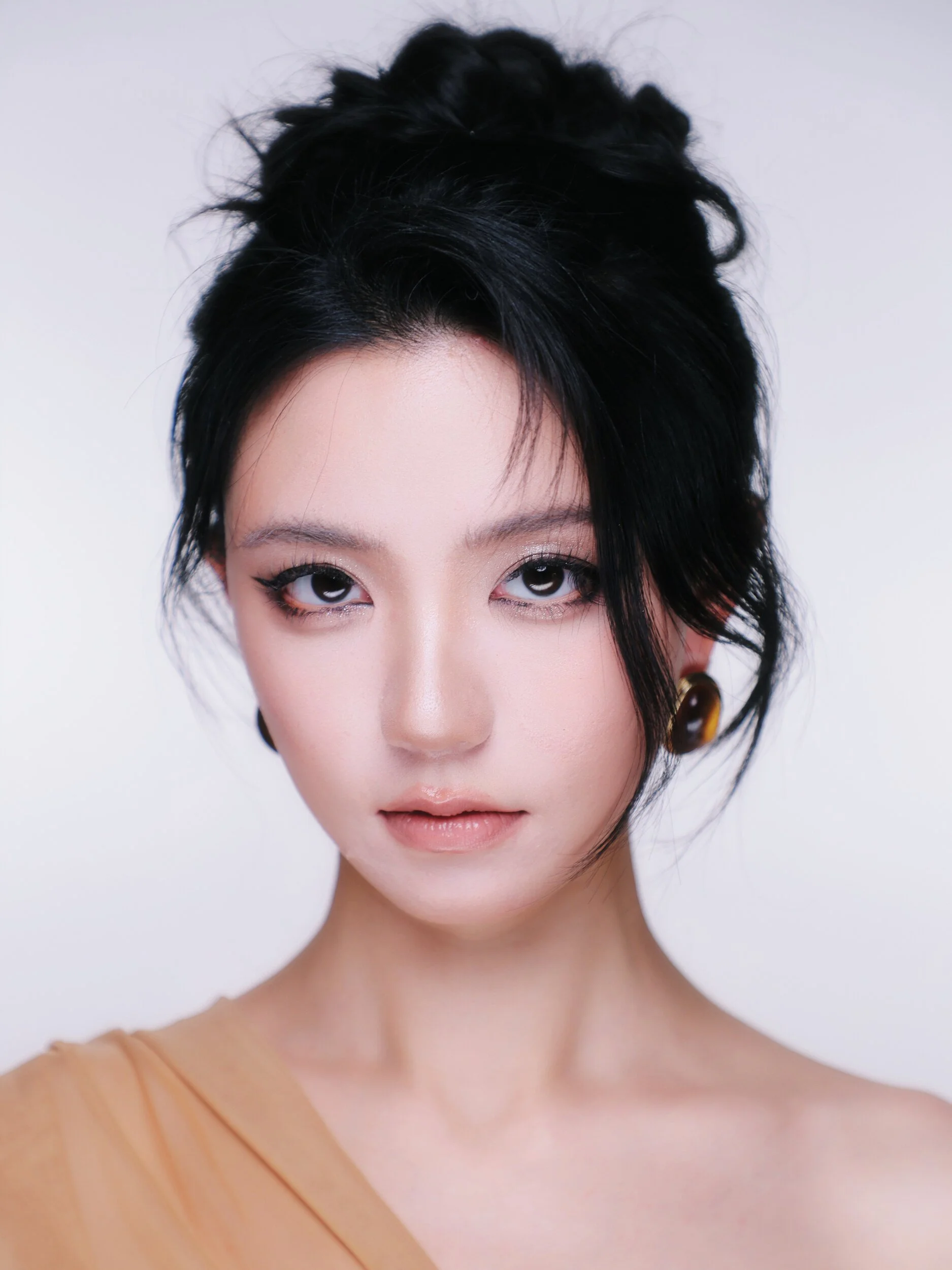 Front-facing beauty portrait of the same model with a textured updo, soft flushed skin and amber earrings
