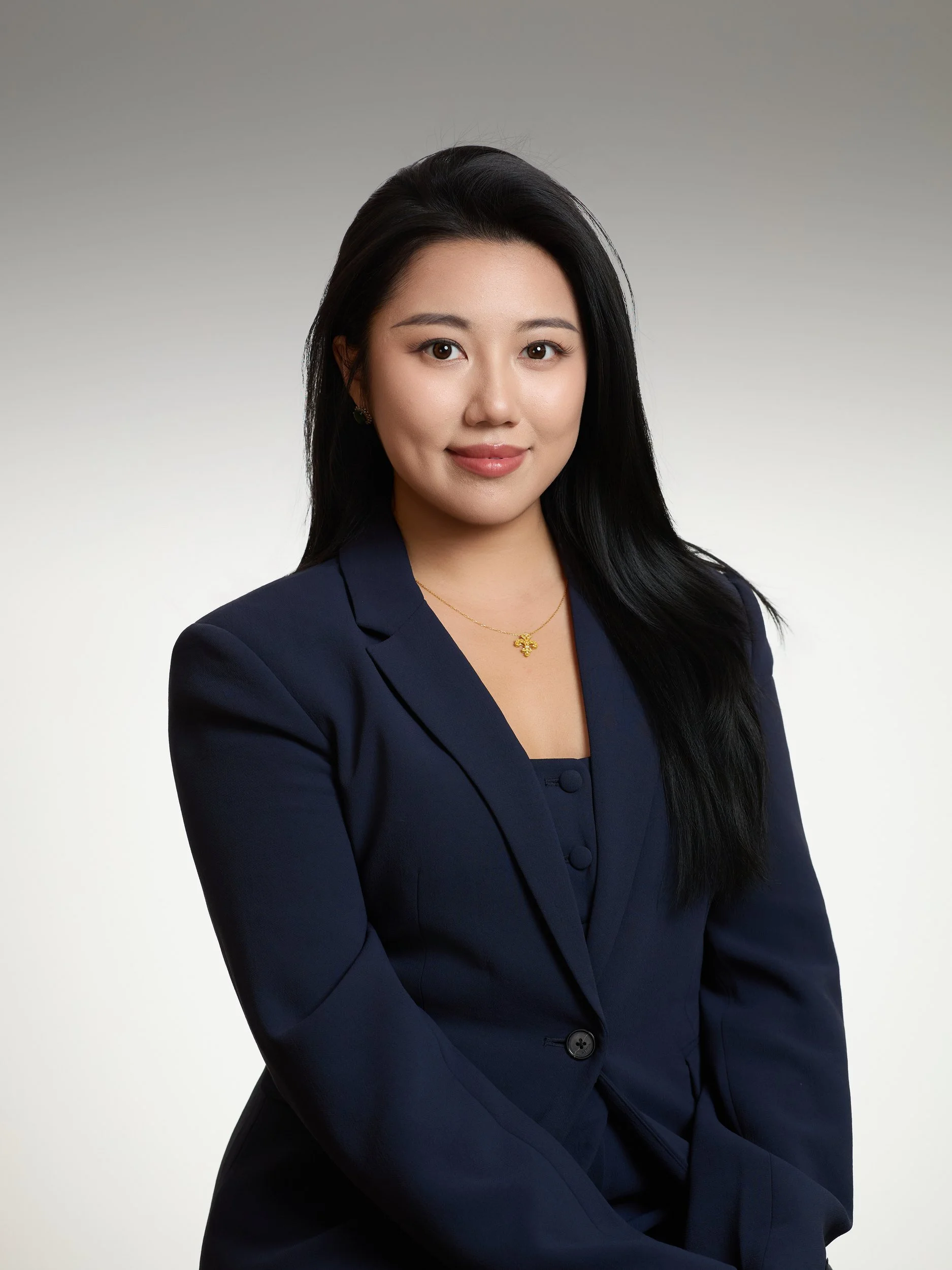 Corporate headshot of a woman in a navy blazer on a grey gradient