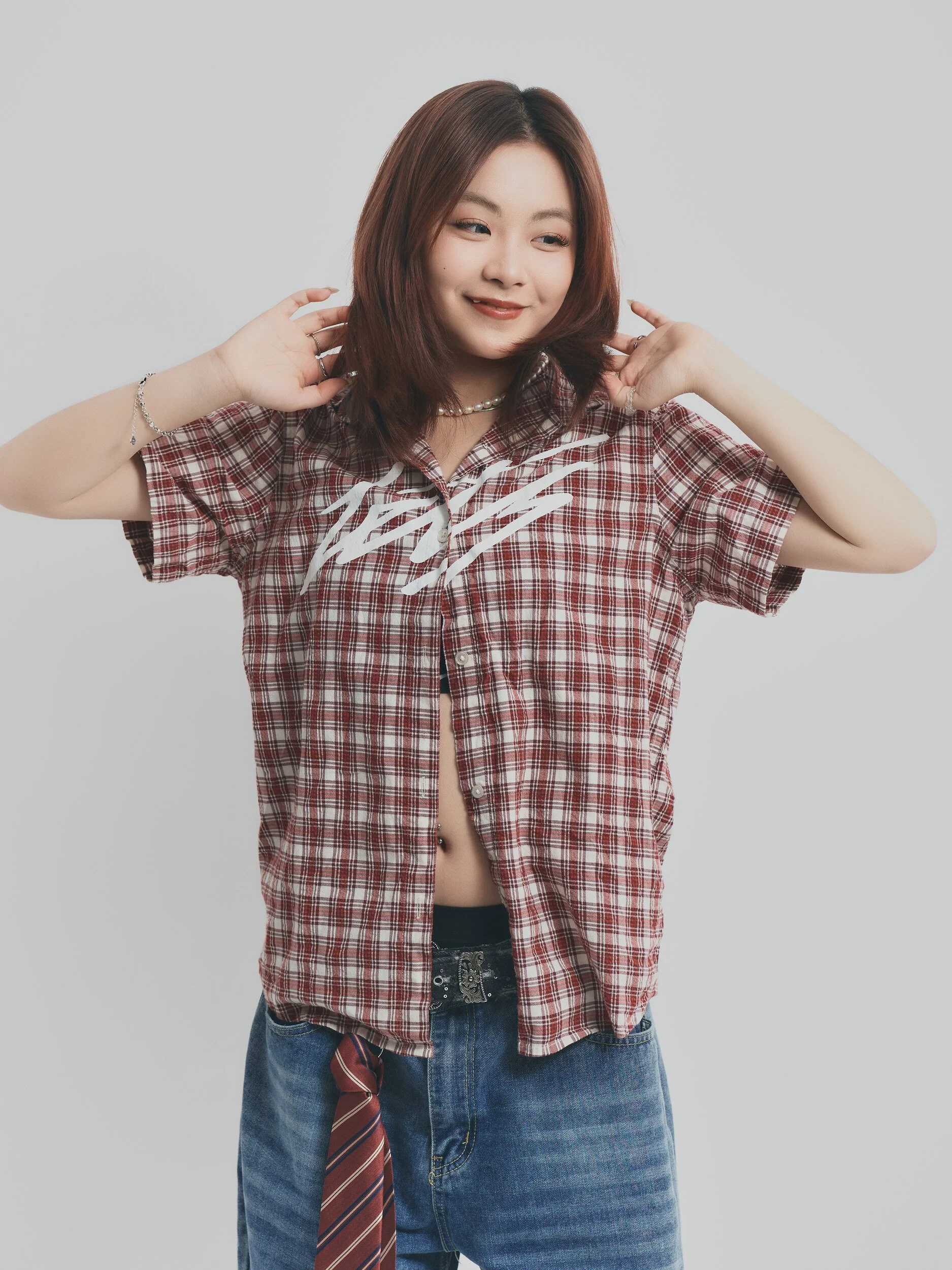 Model test half-length shot of a smiling woman in a red plaid shirt with both hands at her hair