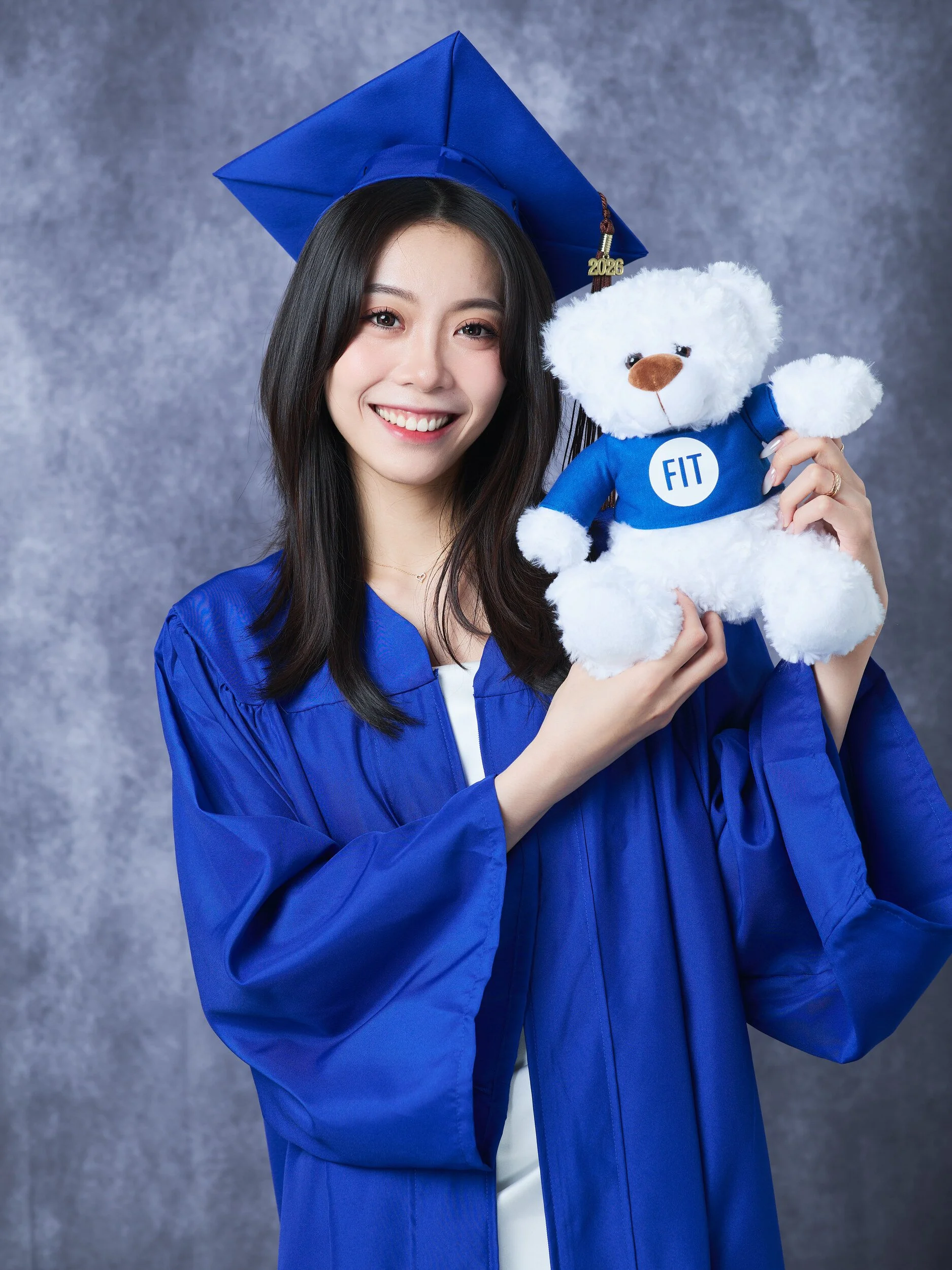 FIT graduation portrait of a woman in a blue gown holding a teddy bear