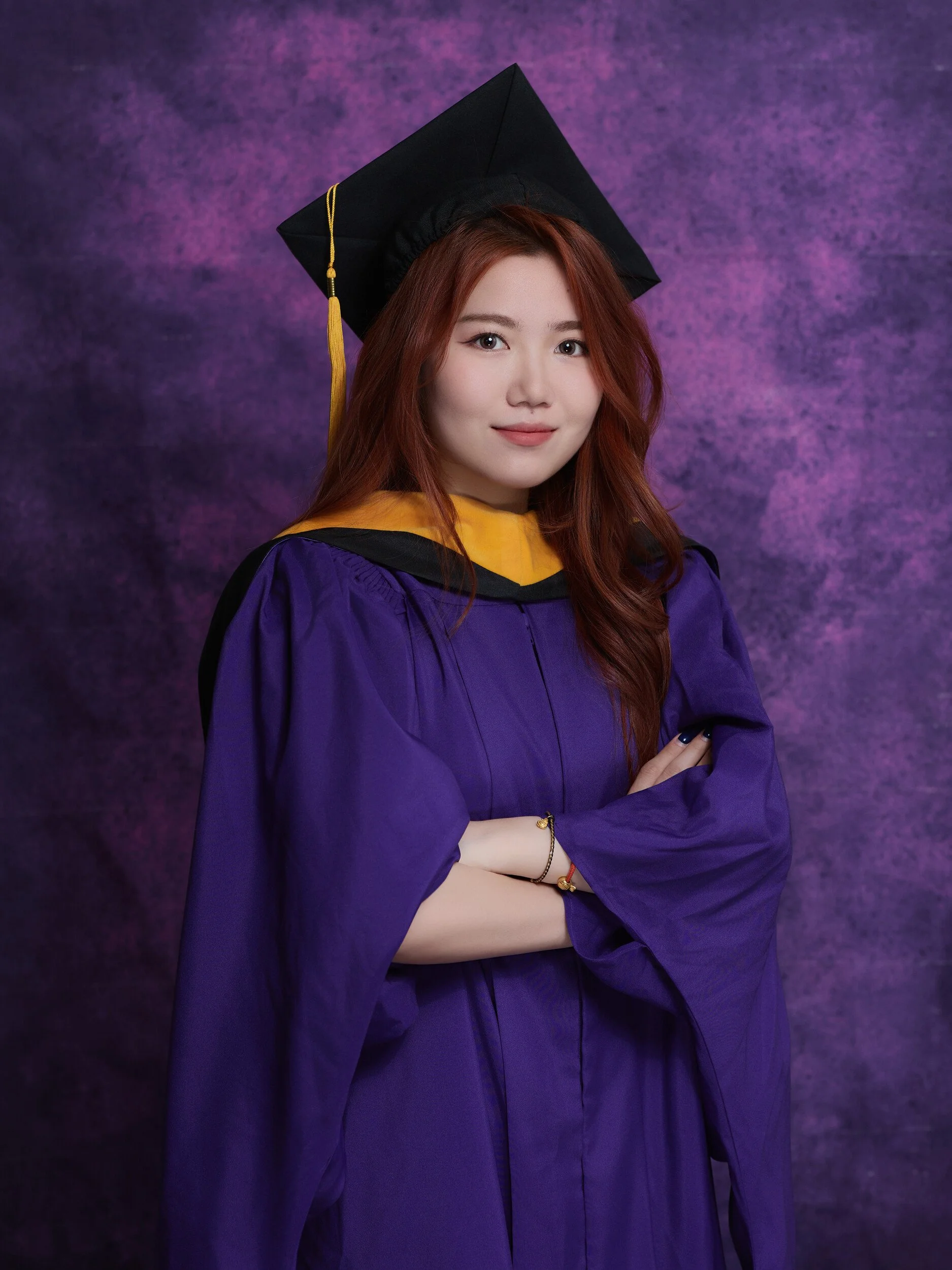 NYU graduation portrait of a woman with red hair and a gold hood, arms crossed