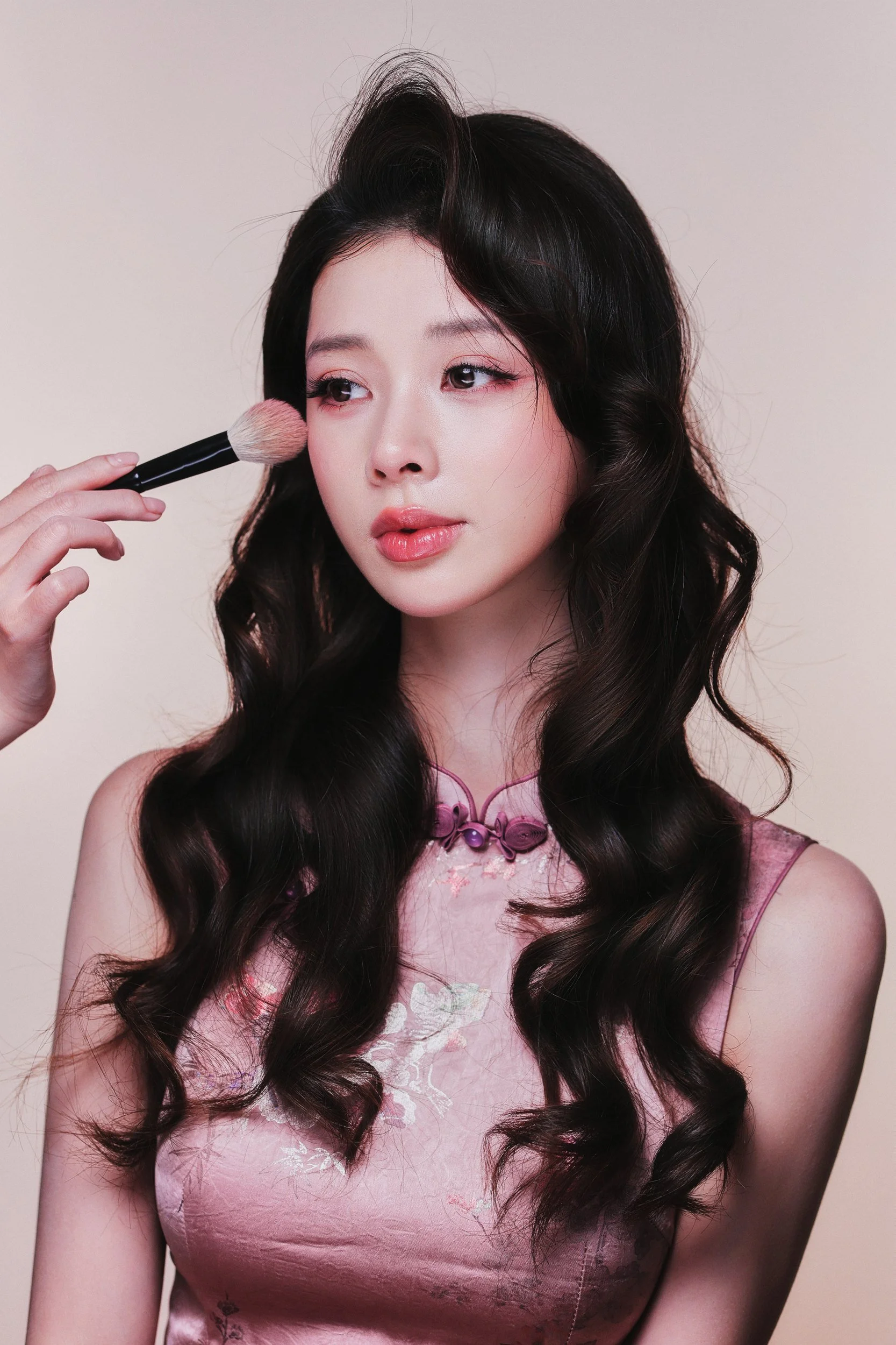 Studio portrait of a woman in a pink qipao holding a makeup brush