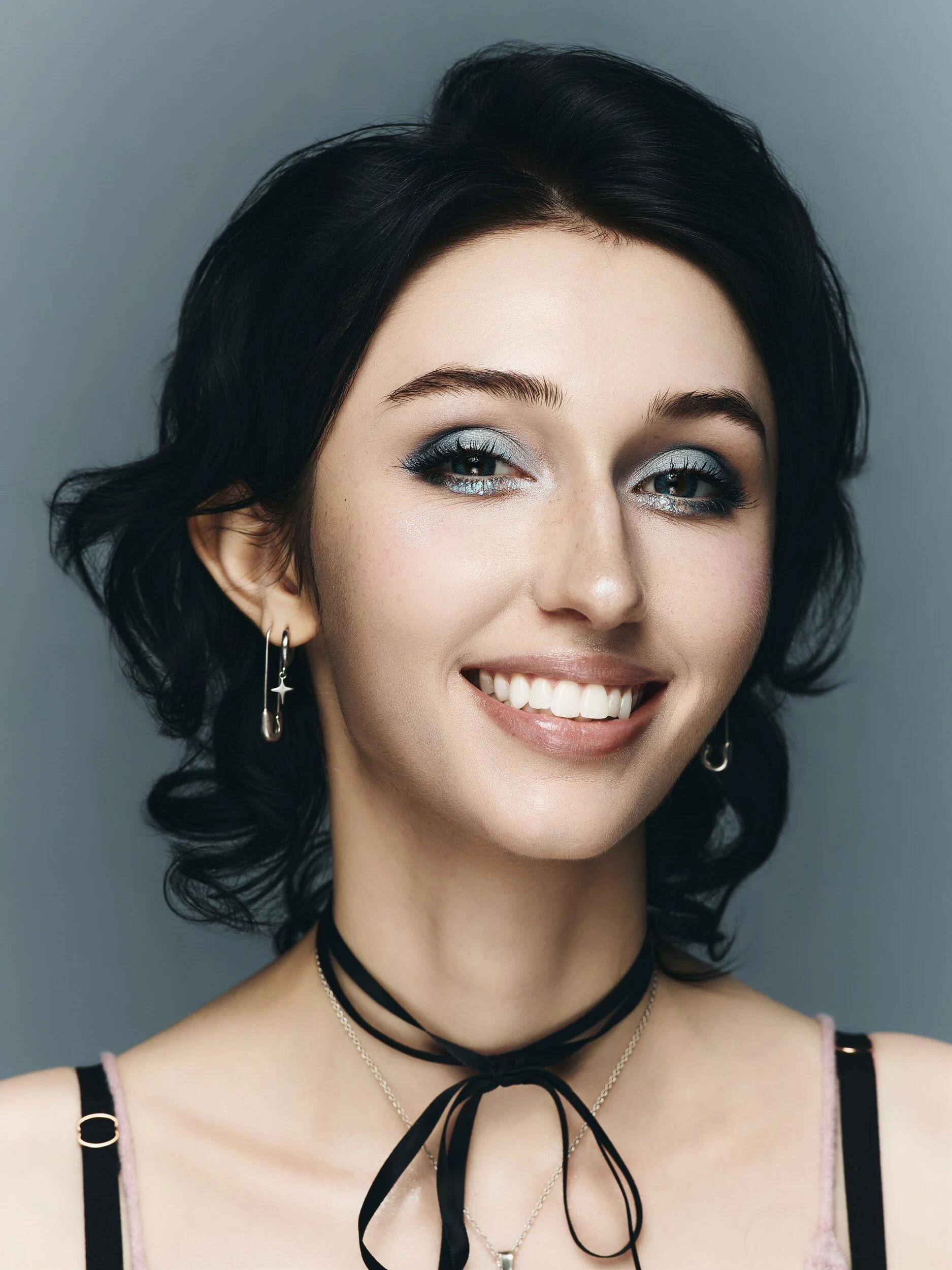 Smiling beauty portrait of the same model with silver-blue eyes and a black ribbon choker on a slate backdrop