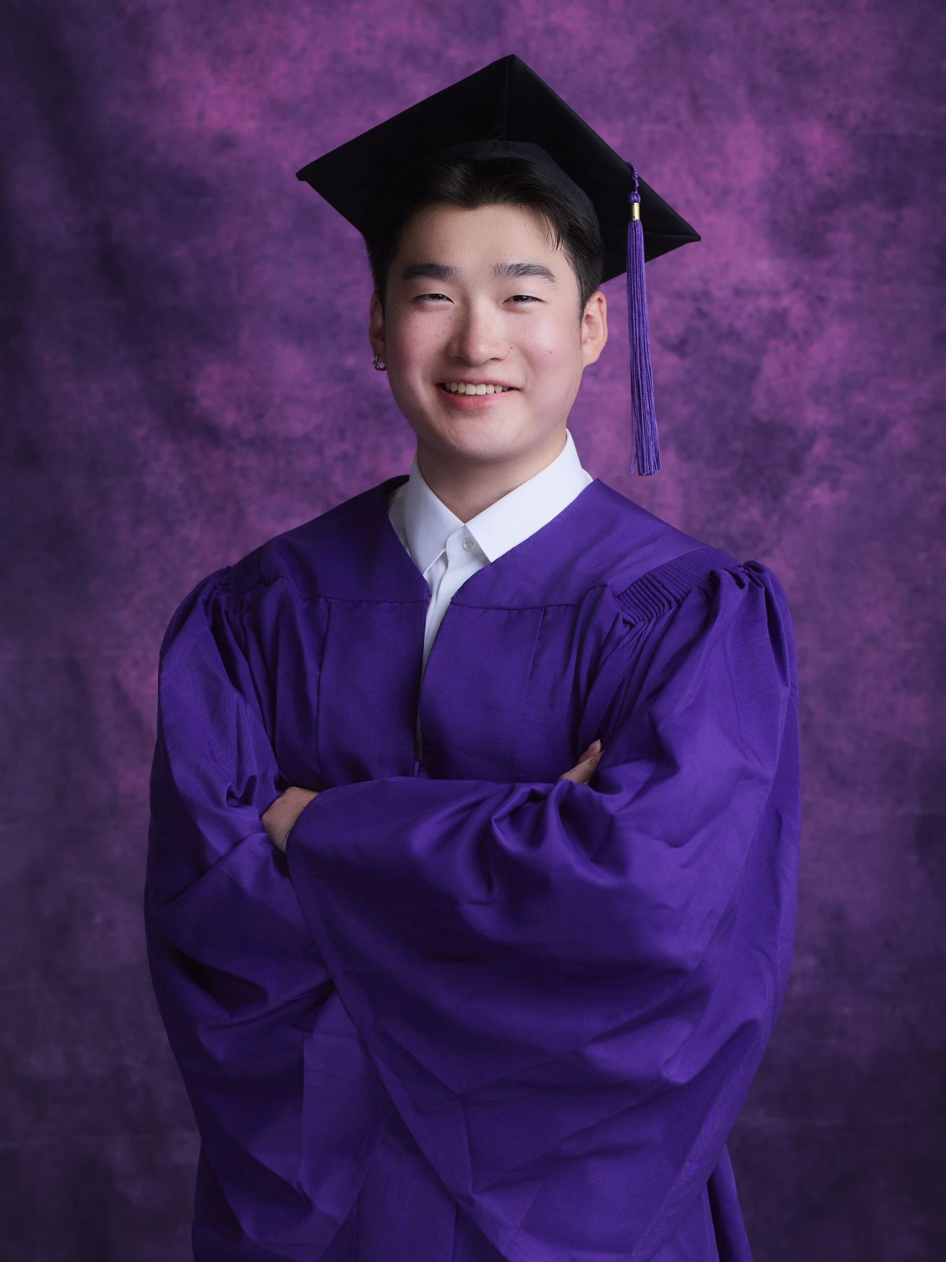 NYU graduation portrait of a smiling young man with arms crossed