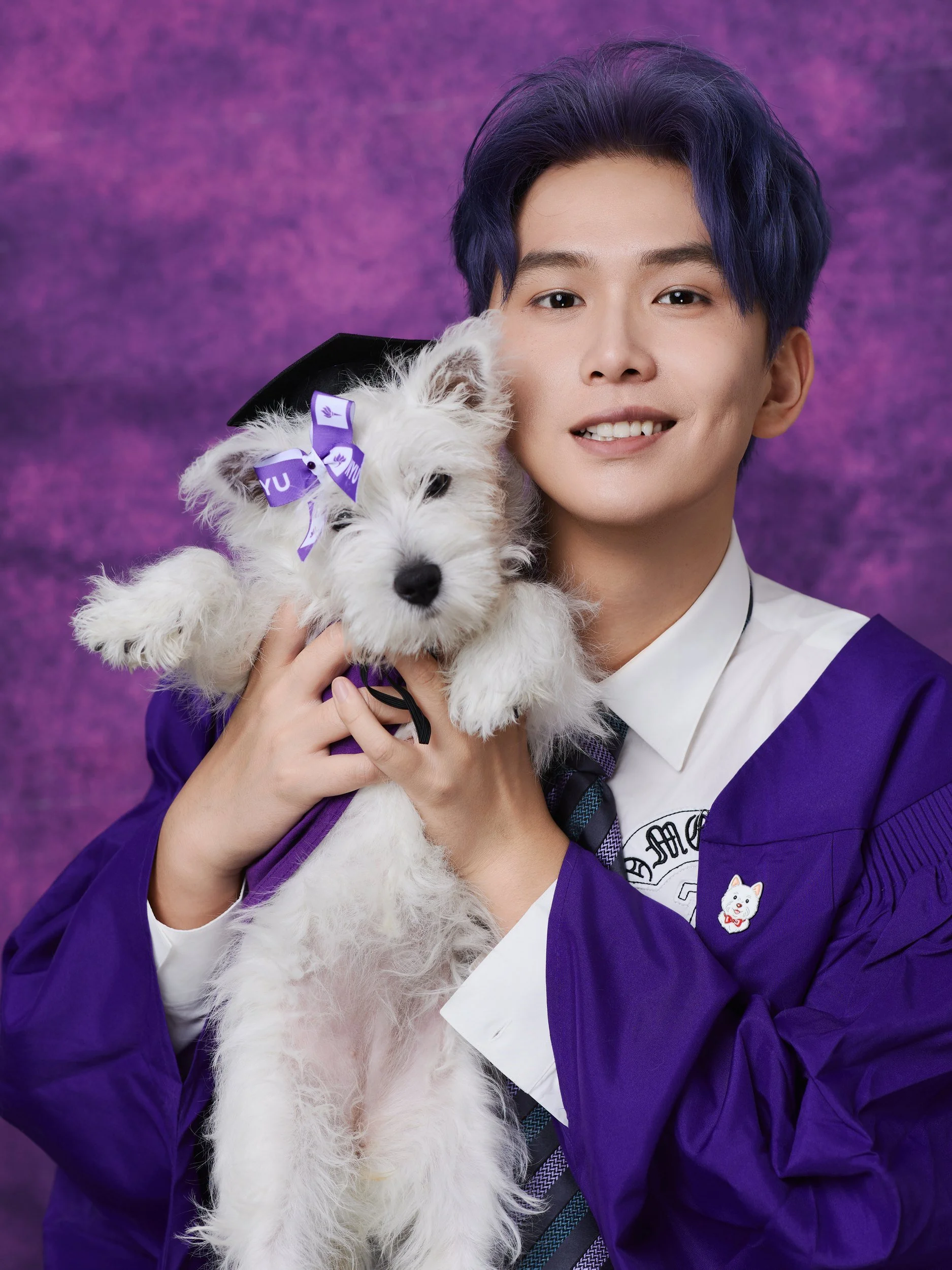 Graduation portrait of a graduate in a purple gown holding a white puppy