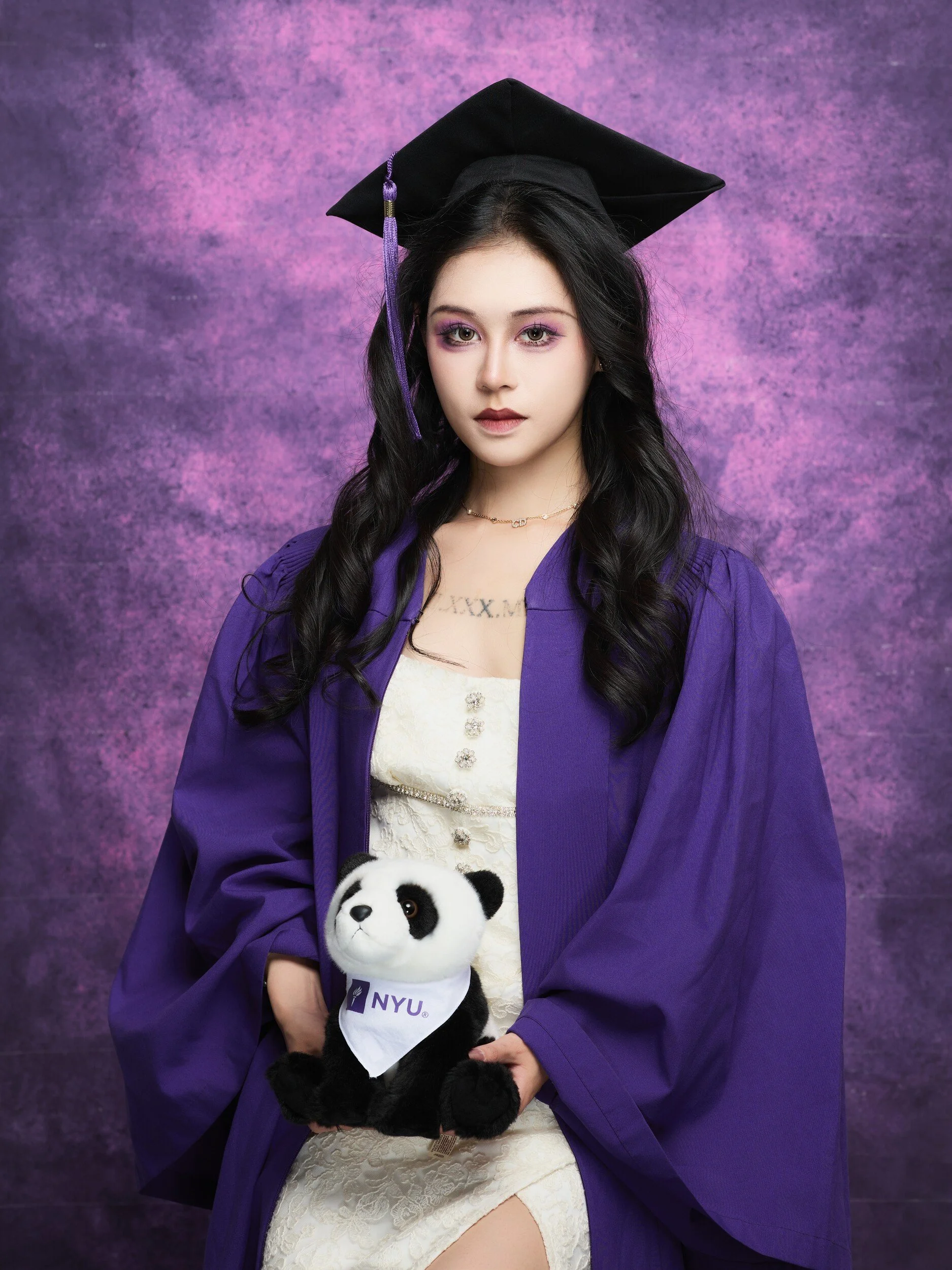 Seated NYU graduation portrait of a woman with long curls and a panda plush