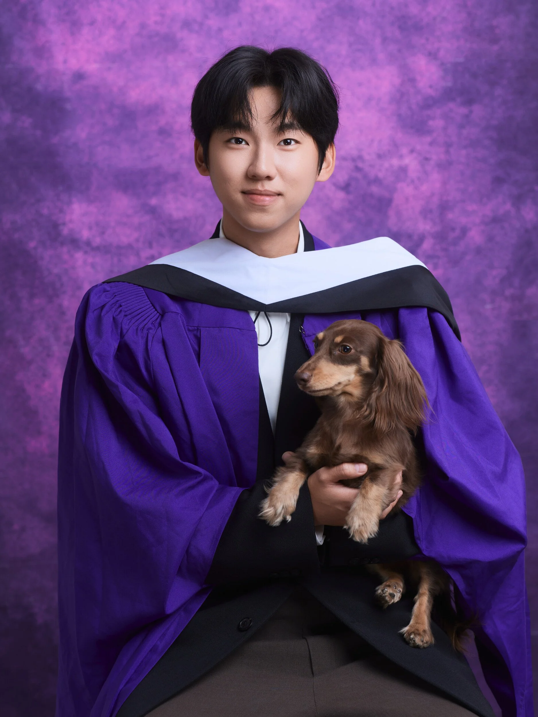 NYU graduation portrait of a young man holding a dachshund