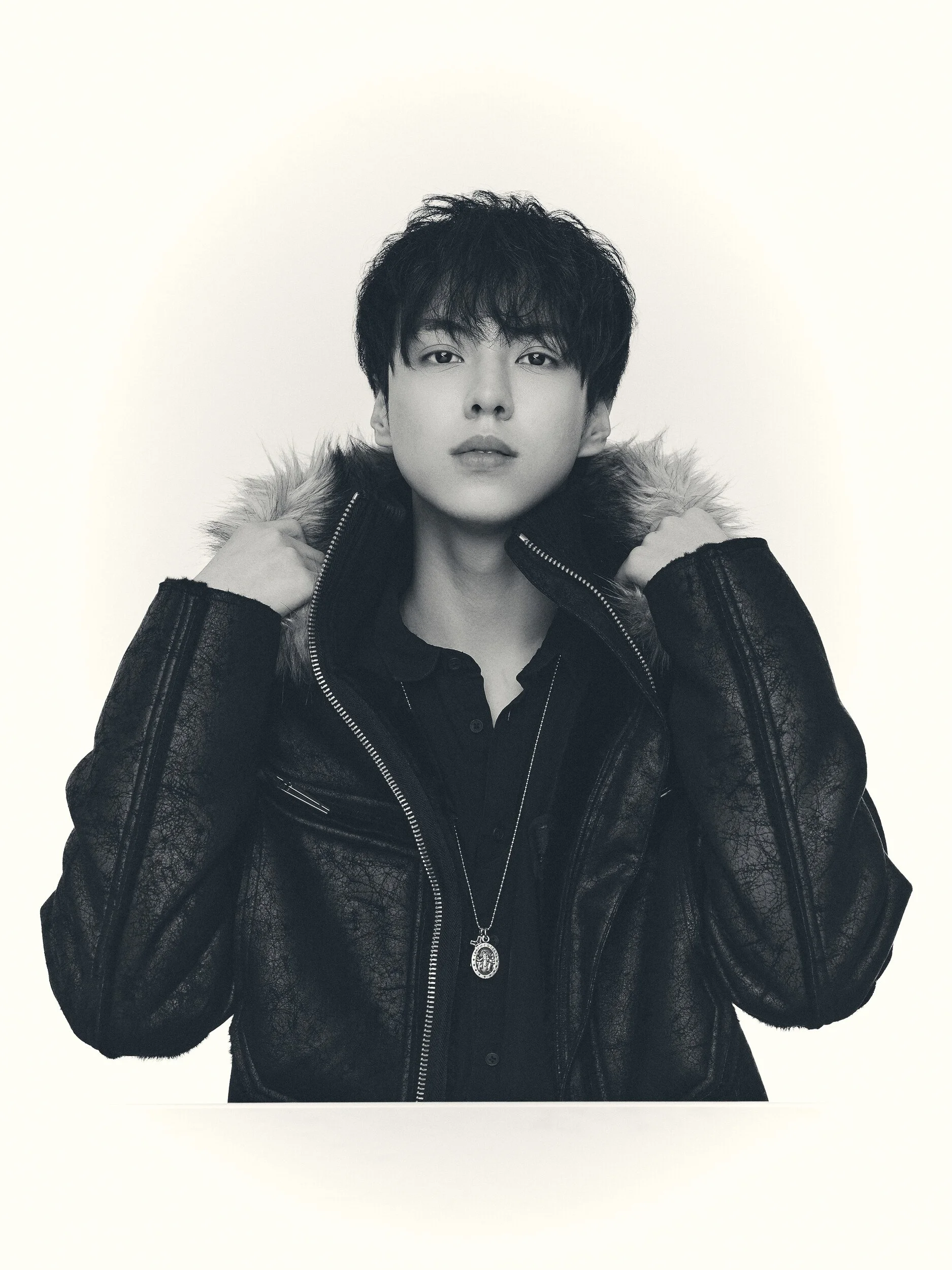 Black and white studio portrait of a man holding the collar of a fur-hooded jacket