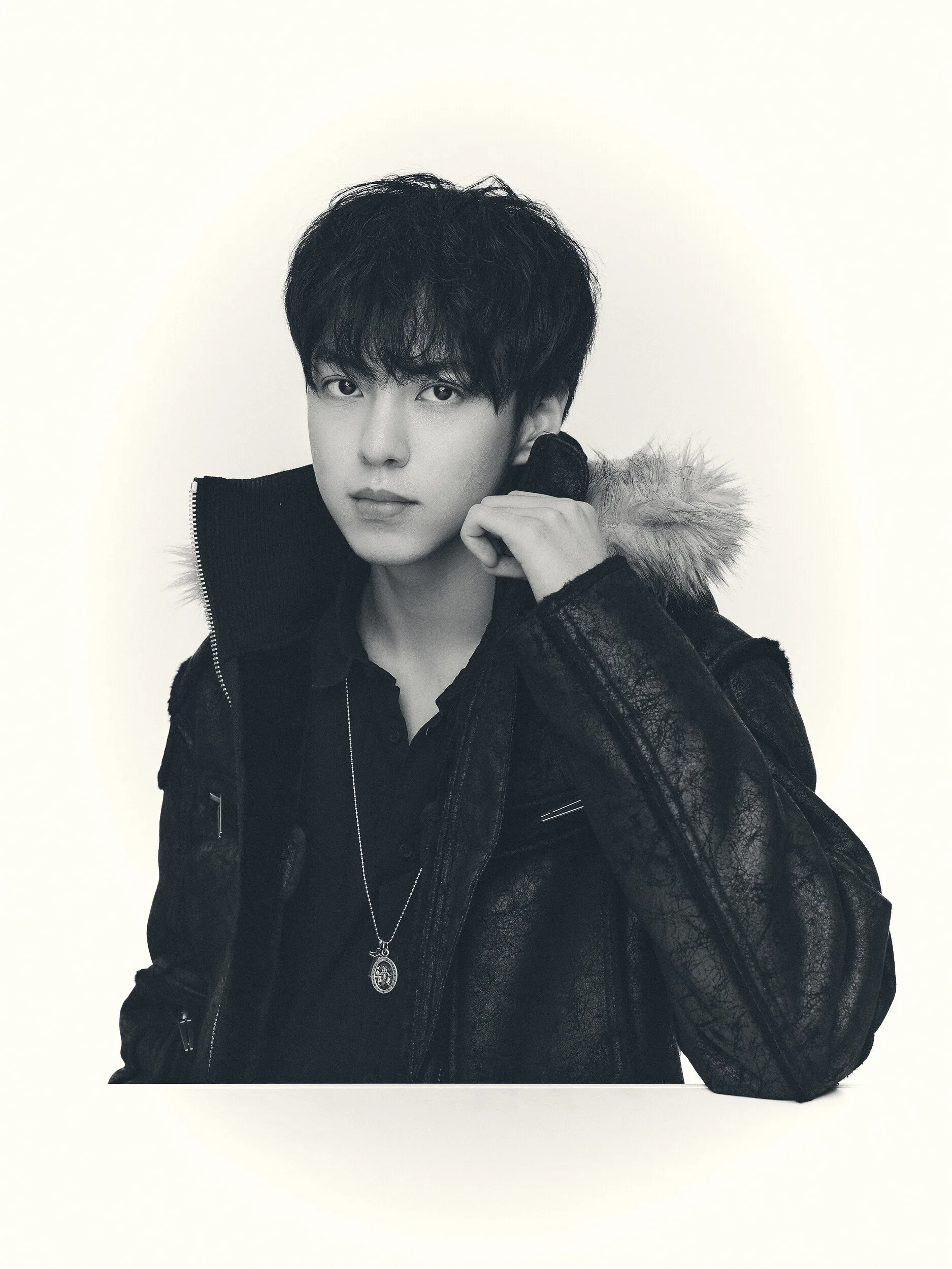 Black and white studio portrait of a man adjusting the collar of a fur-hooded jacket