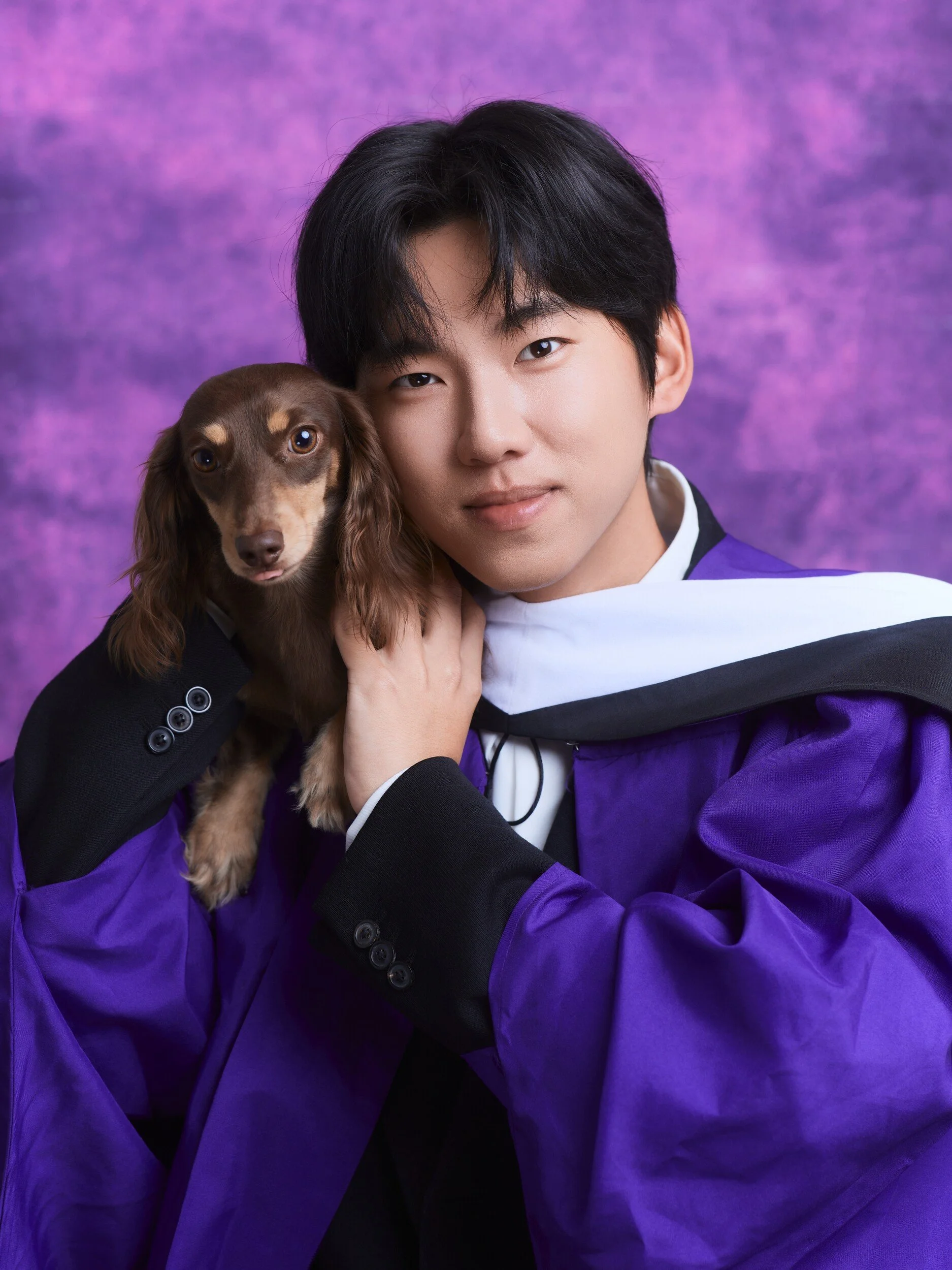 Graduation portrait of a young man hugging his dachshund