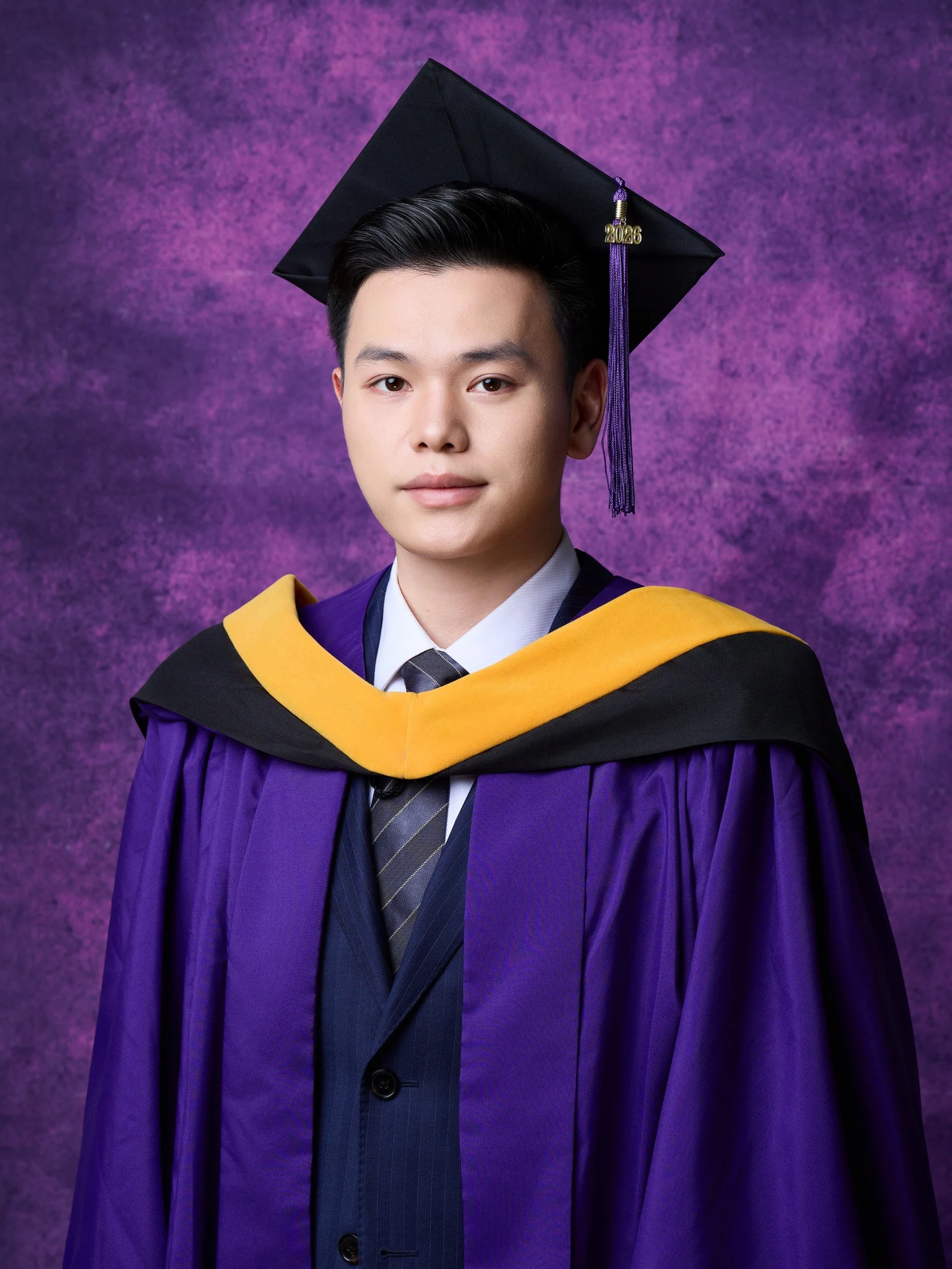 NYU graduation portrait of a man in a purple gown with a gold hood
