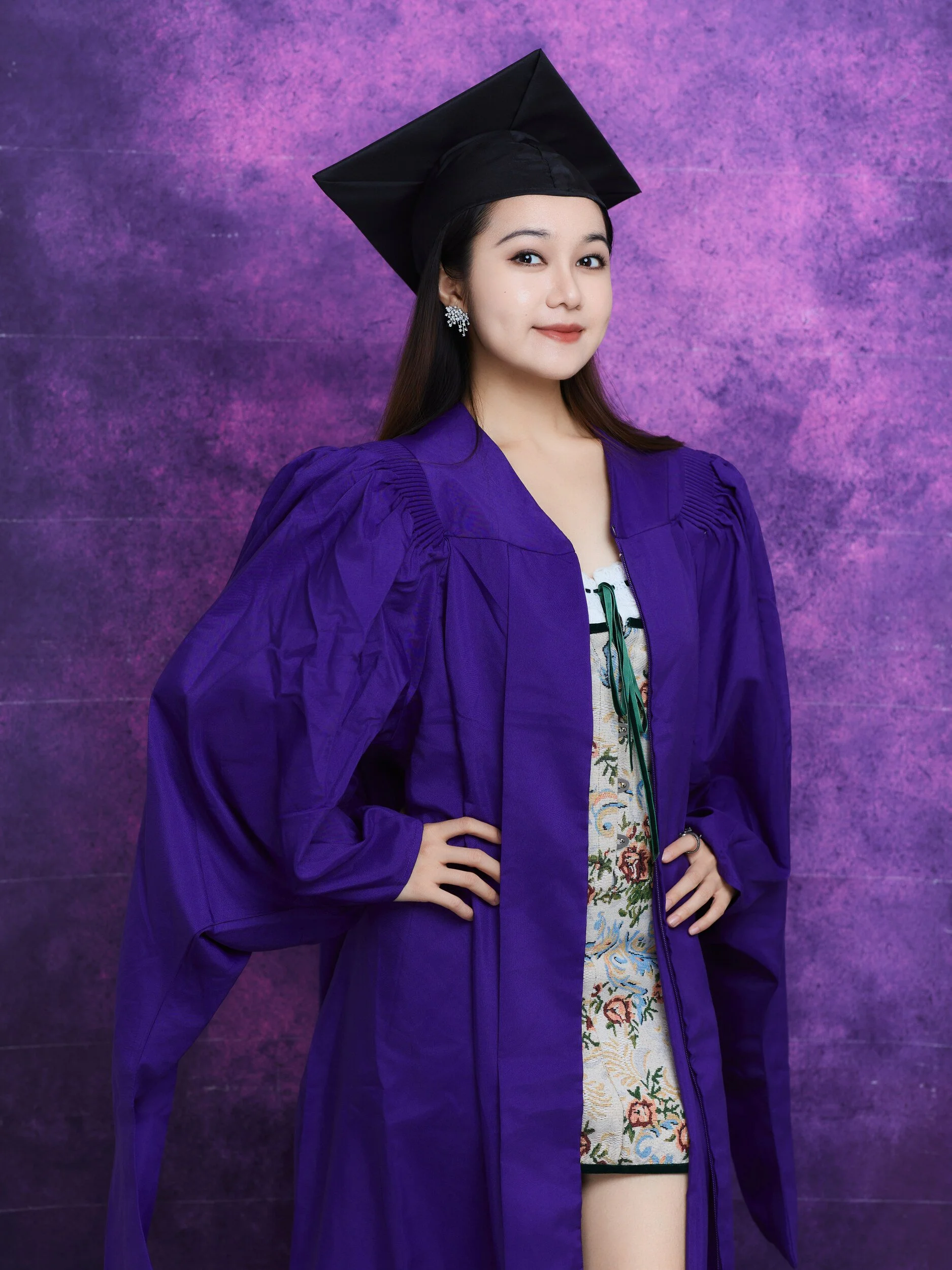 NYU graduation portrait of a woman in a floral dress with a hand on her hip, holding her cap