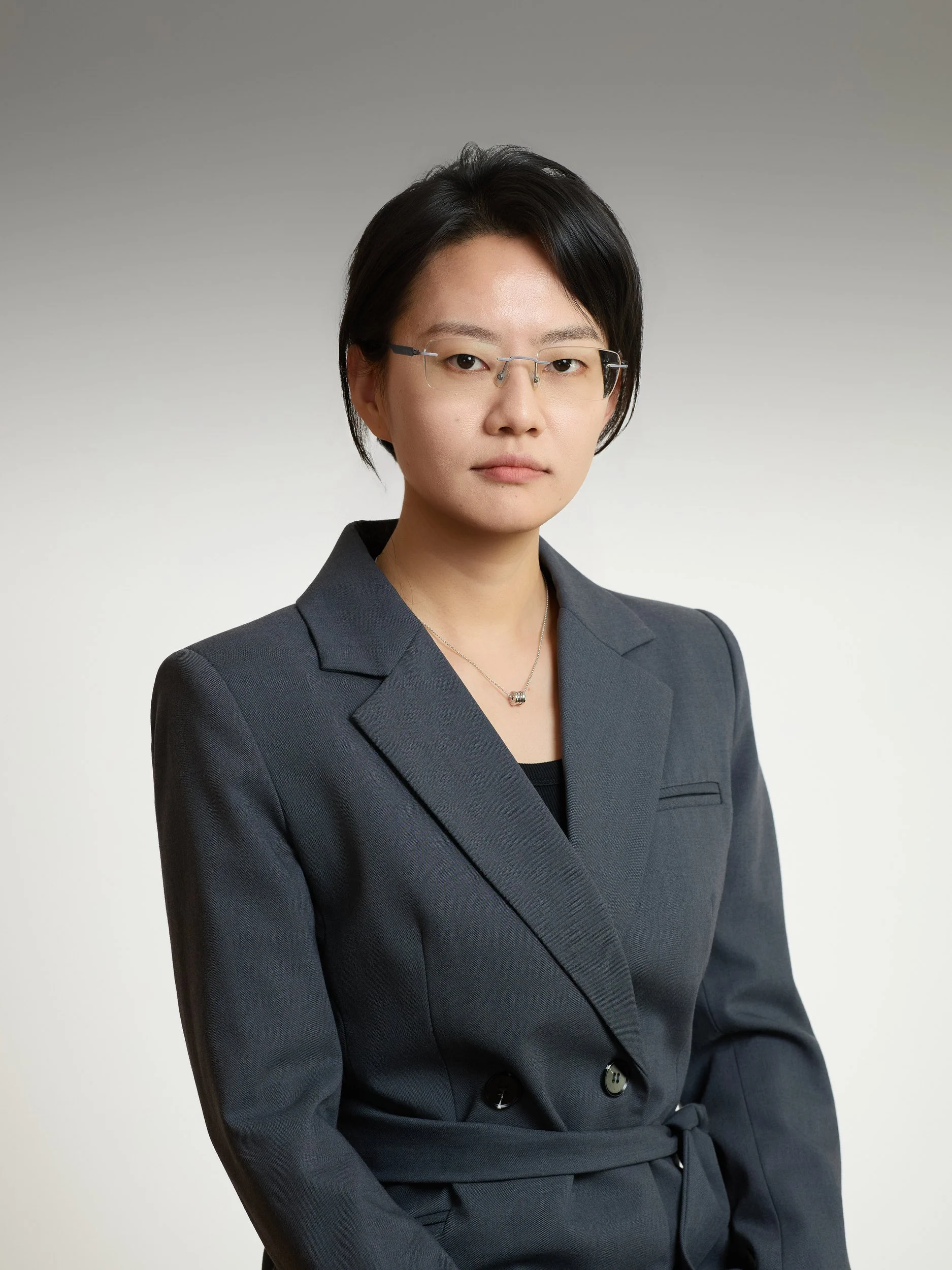 Corporate headshot of a woman with glasses in a grey belted blazer