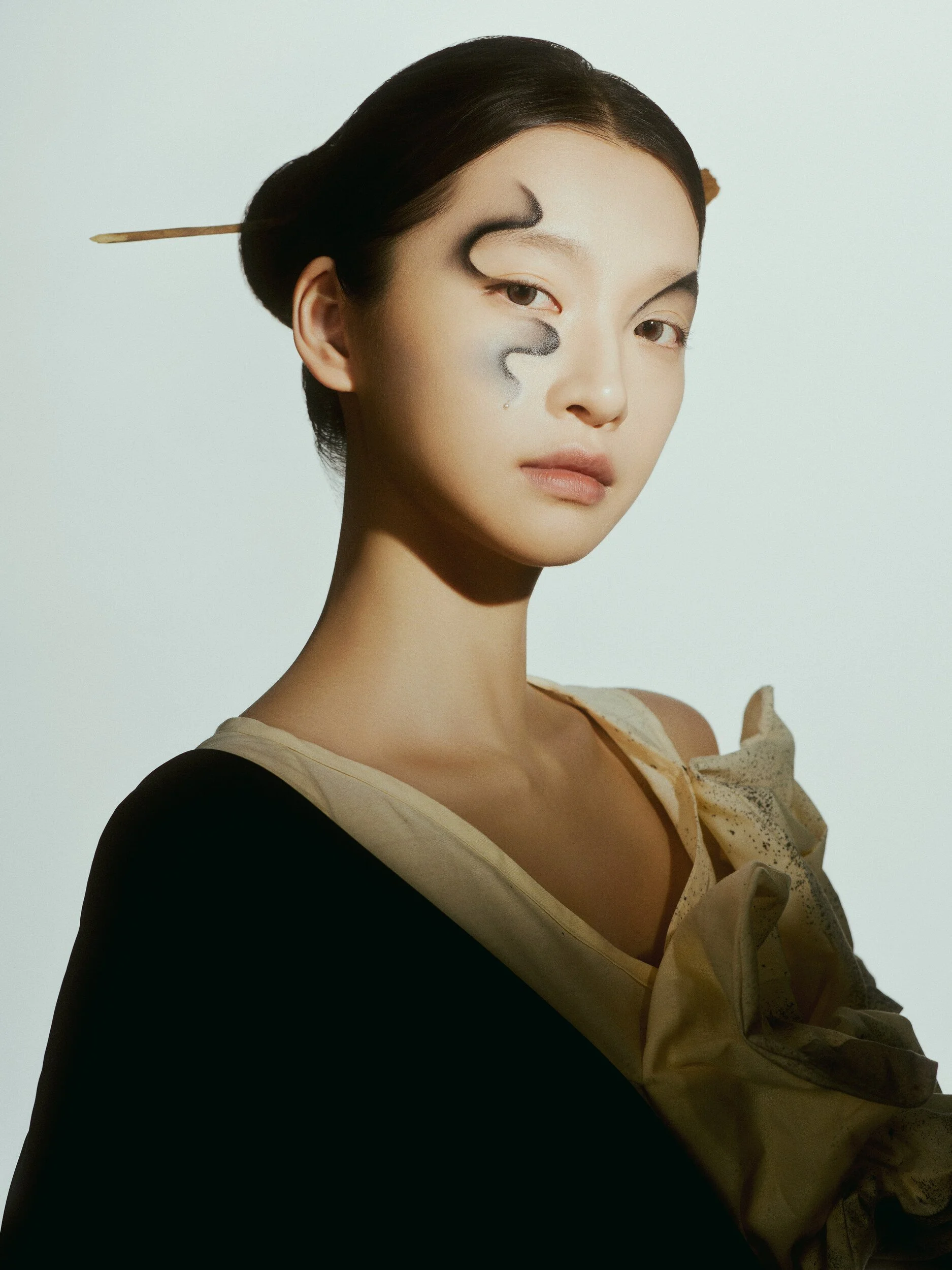 Half-length beauty portrait with painted ink-wave face art and a hairpin, wearing a black and cream ruffled top