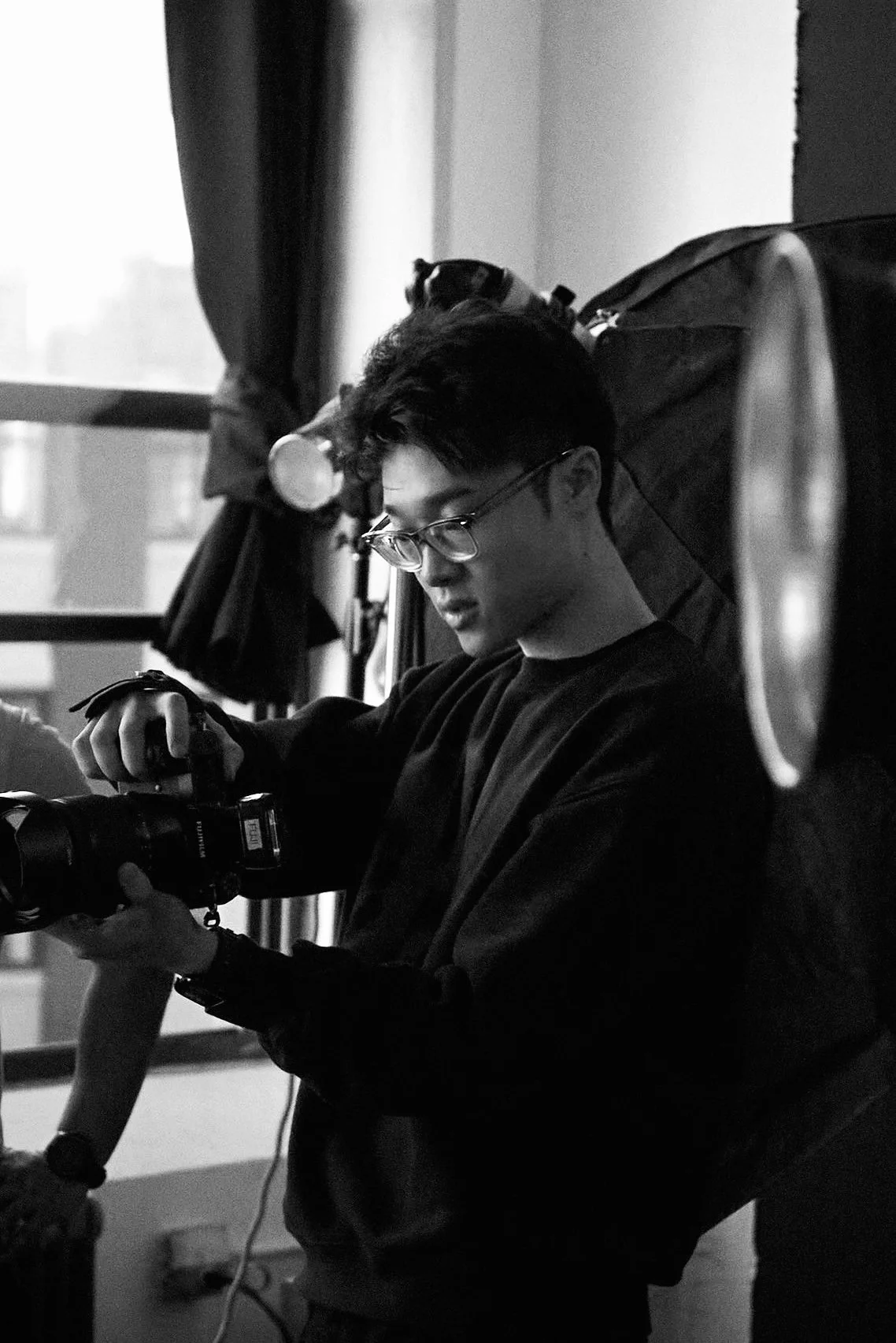Ziyang Wang working with a camera in a photography studio, black-and-white portrait.