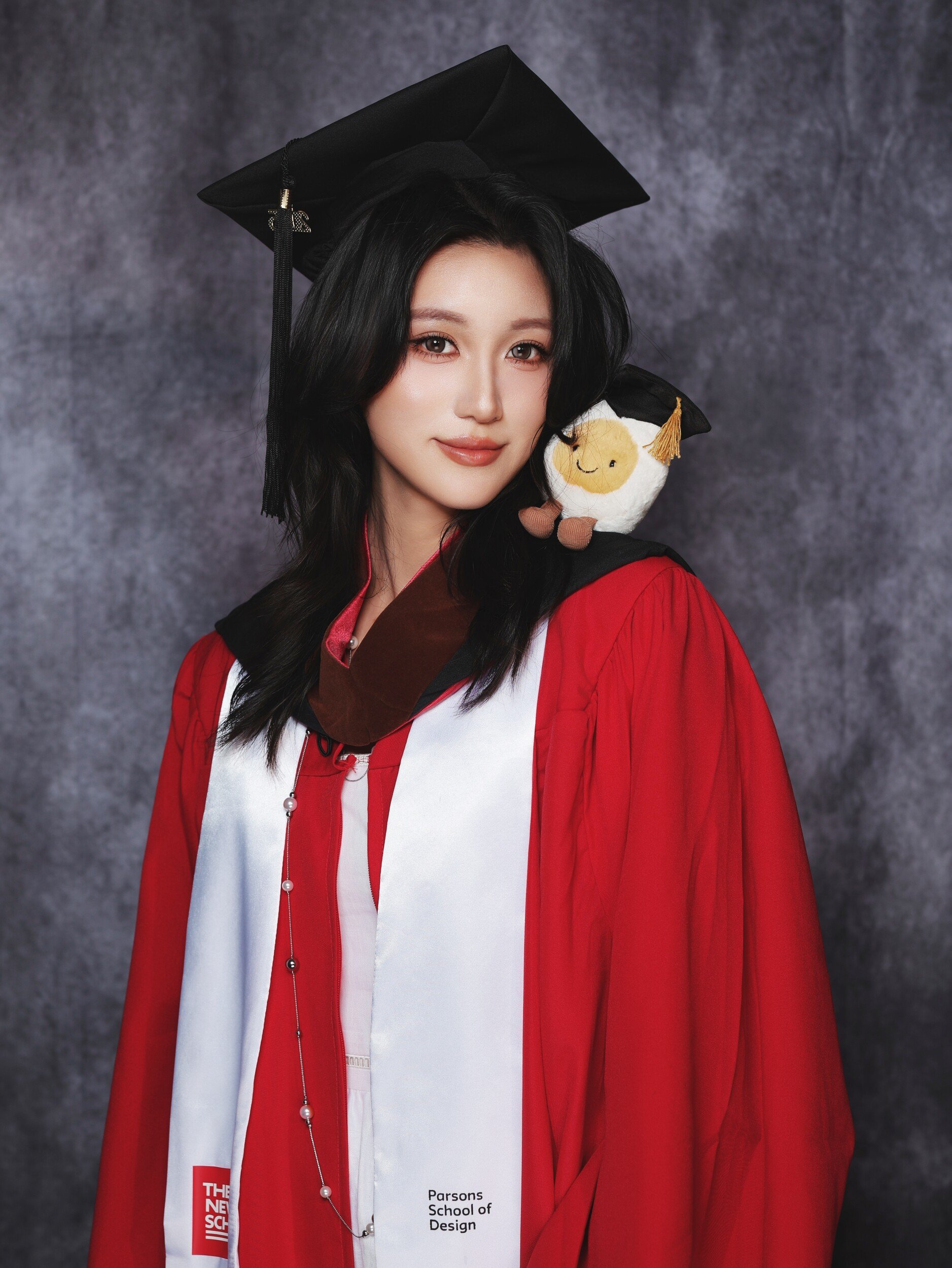 Parsons graduate in a red gown with a plush toy on her shoulder
