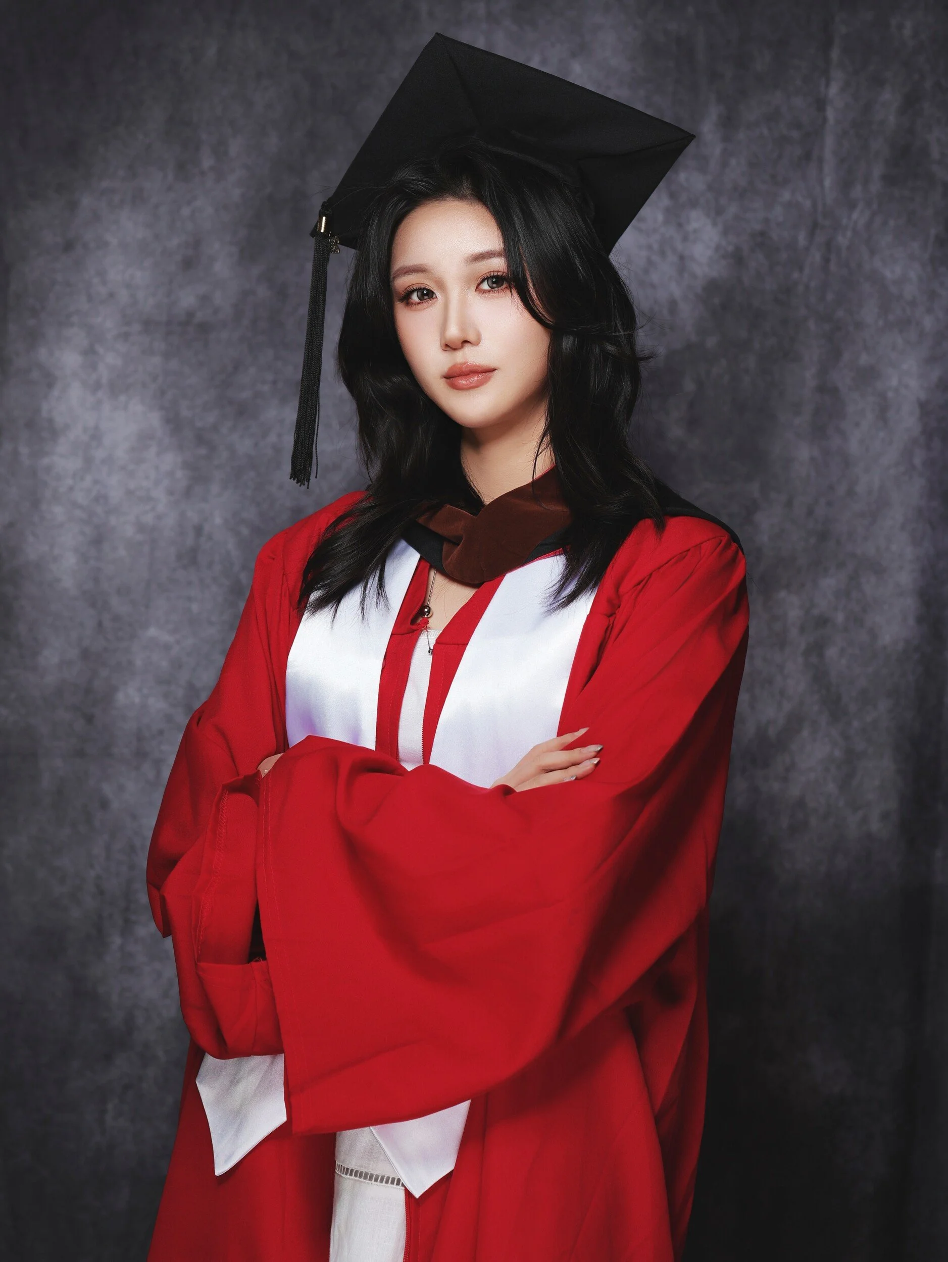 Parsons graduate in a red gown, arms crossed