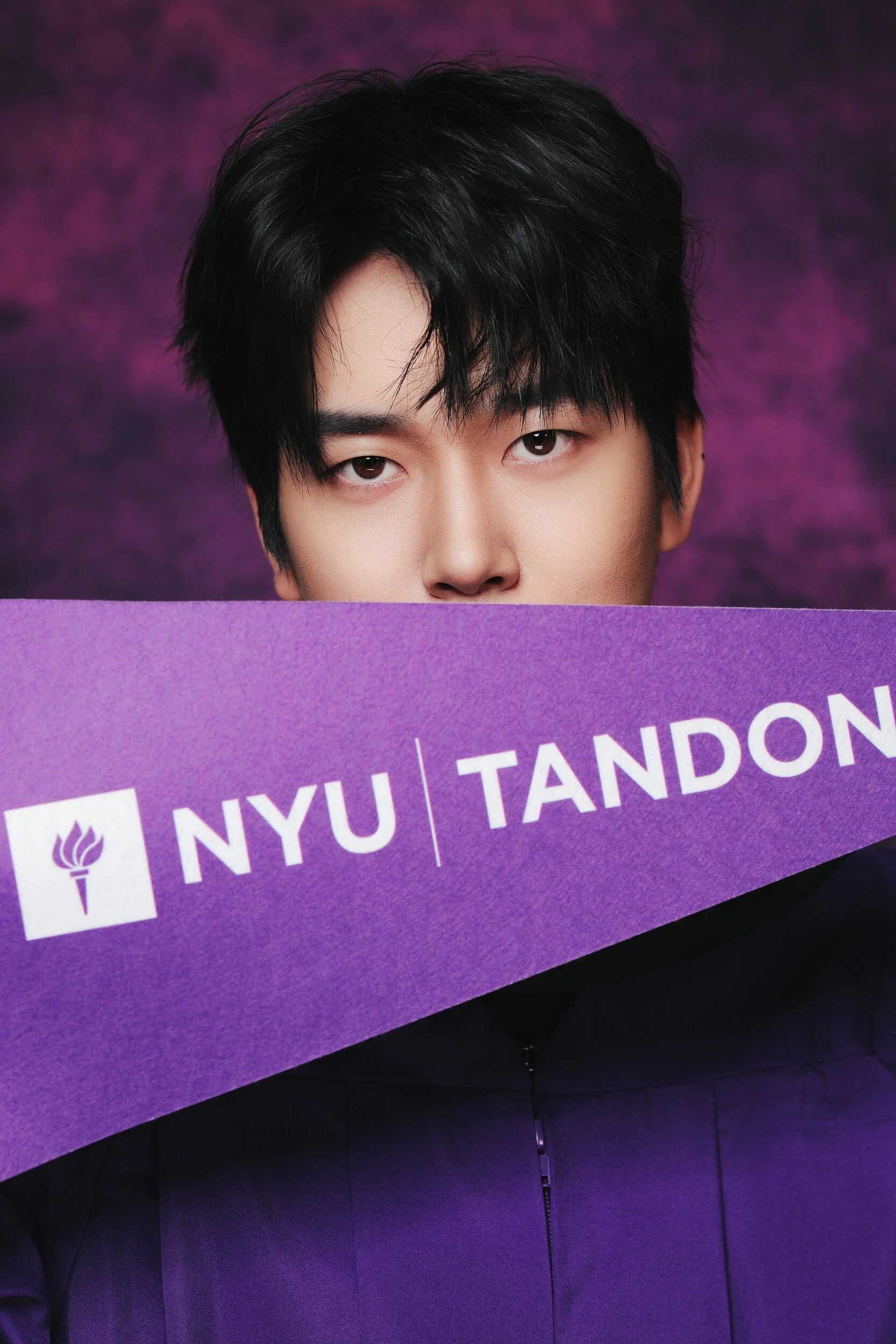 NYU Tandon graduate holding a purple pennant below his eyes