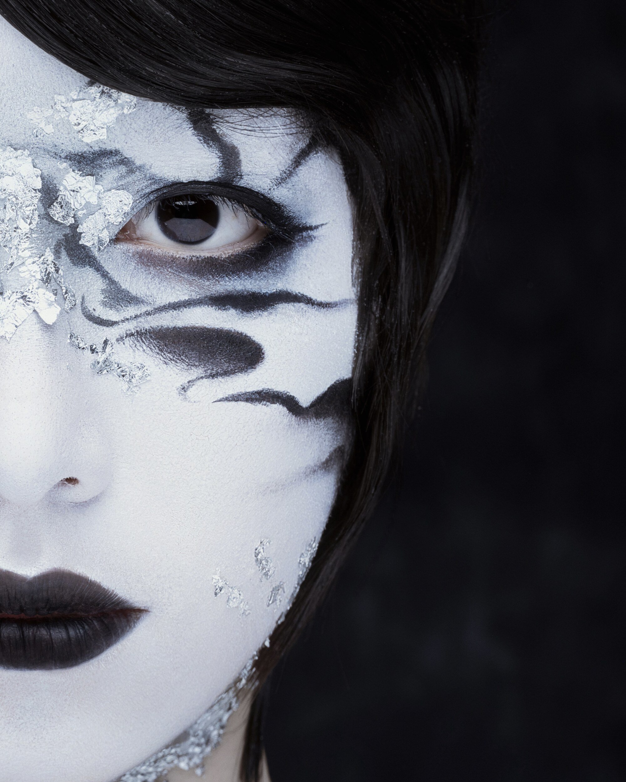 Detail of the same look: silver leaf and black ink strokes around one eye on white-painted skin