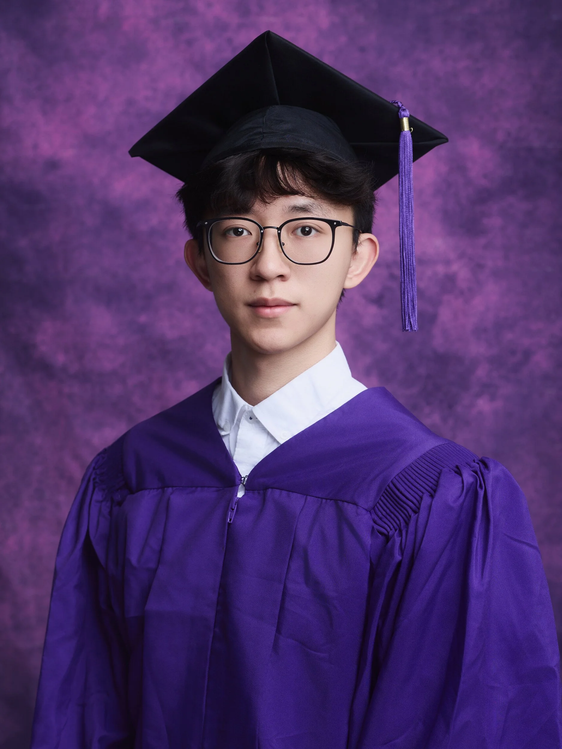 NYU graduation portrait of a young man with glasses in a purple gown and cap