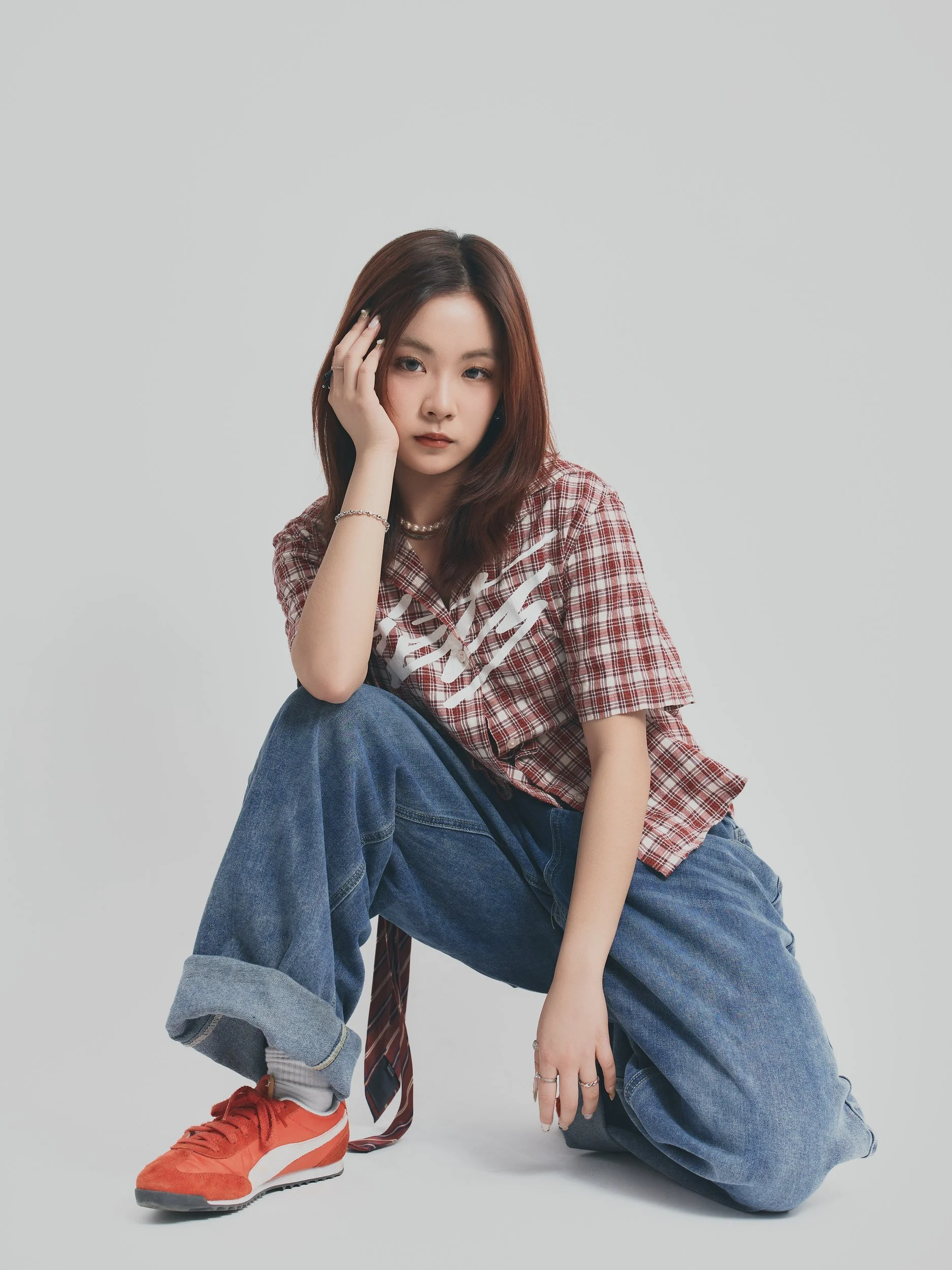 Model test shot of a woman kneeling in a plaid shirt and red sneakers