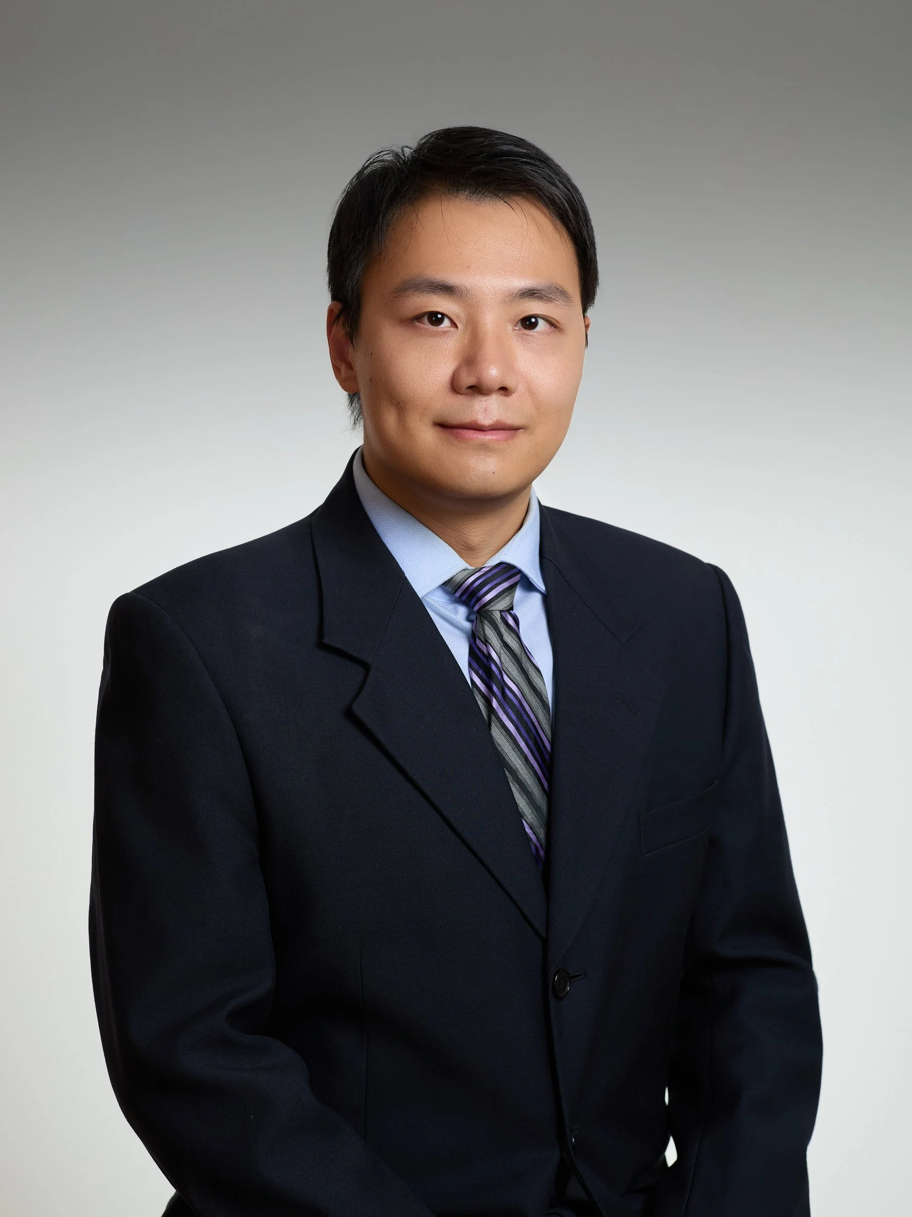 Corporate headshot of a man in a dark suit and striped tie on a grey gradient