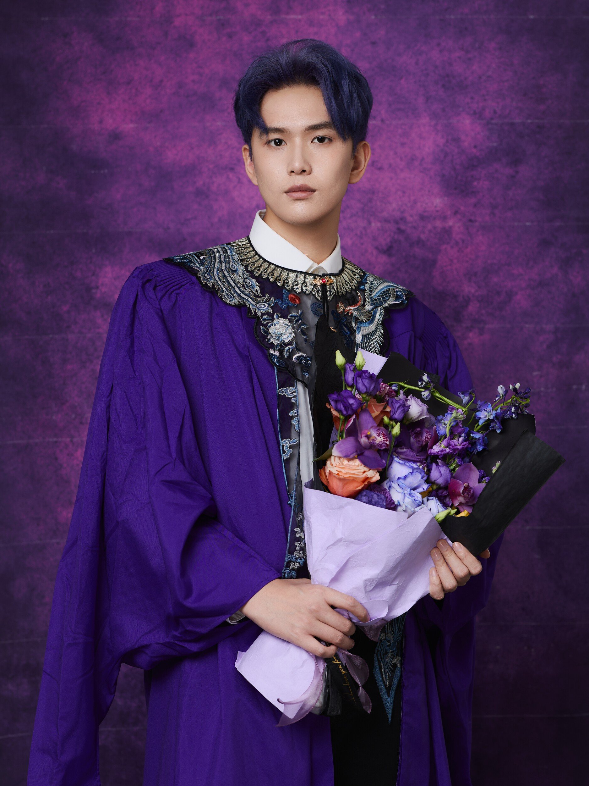Graduate with blue-toned hair holding a purple bouquet
