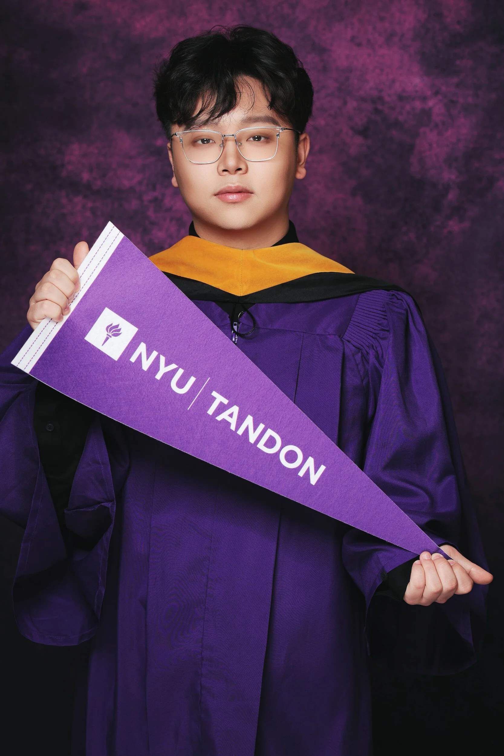 NYU Tandon graduation portrait of a young man with glasses holding a school pennant