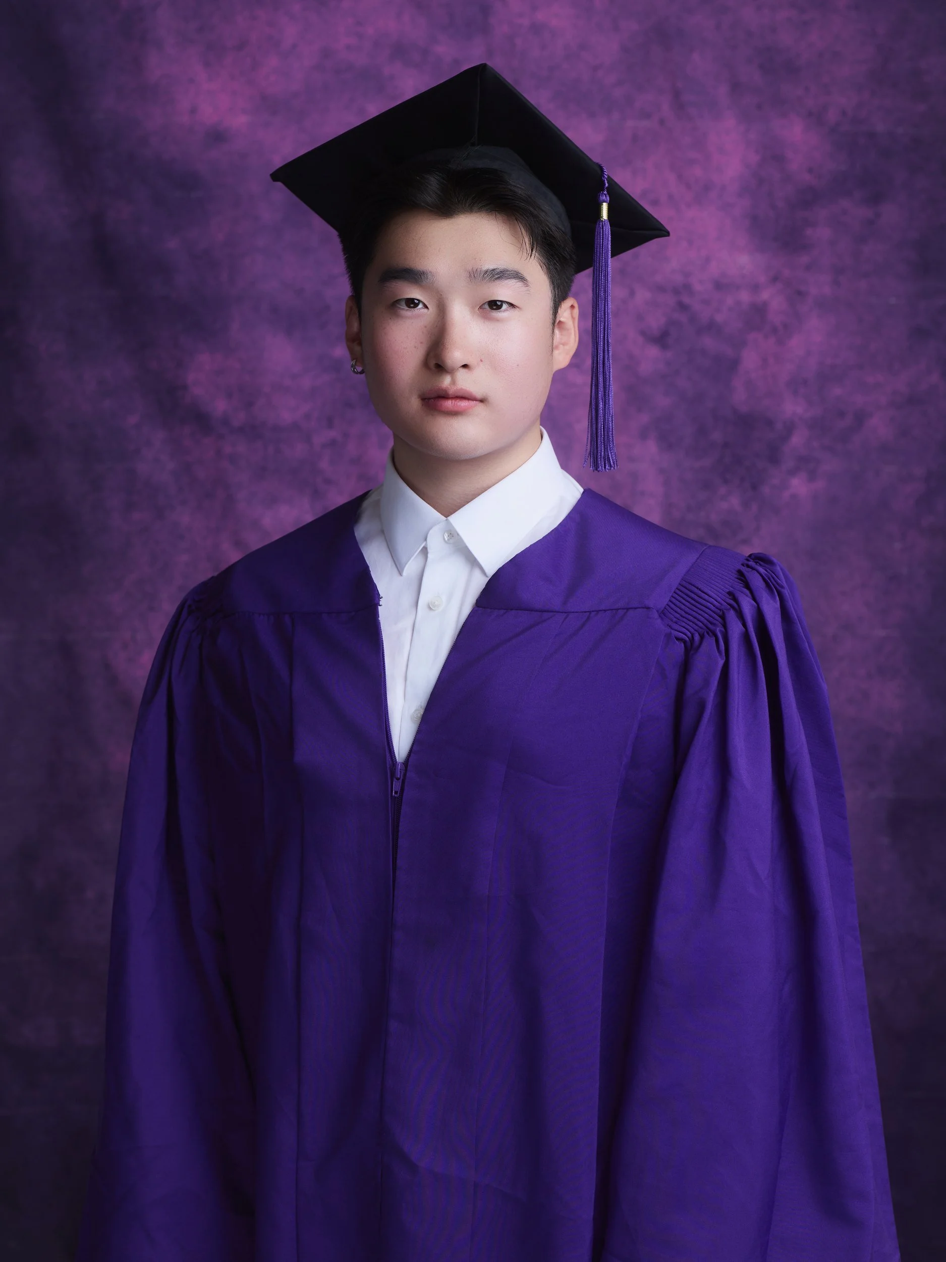 NYU graduation portrait of a man in a purple gown and cap