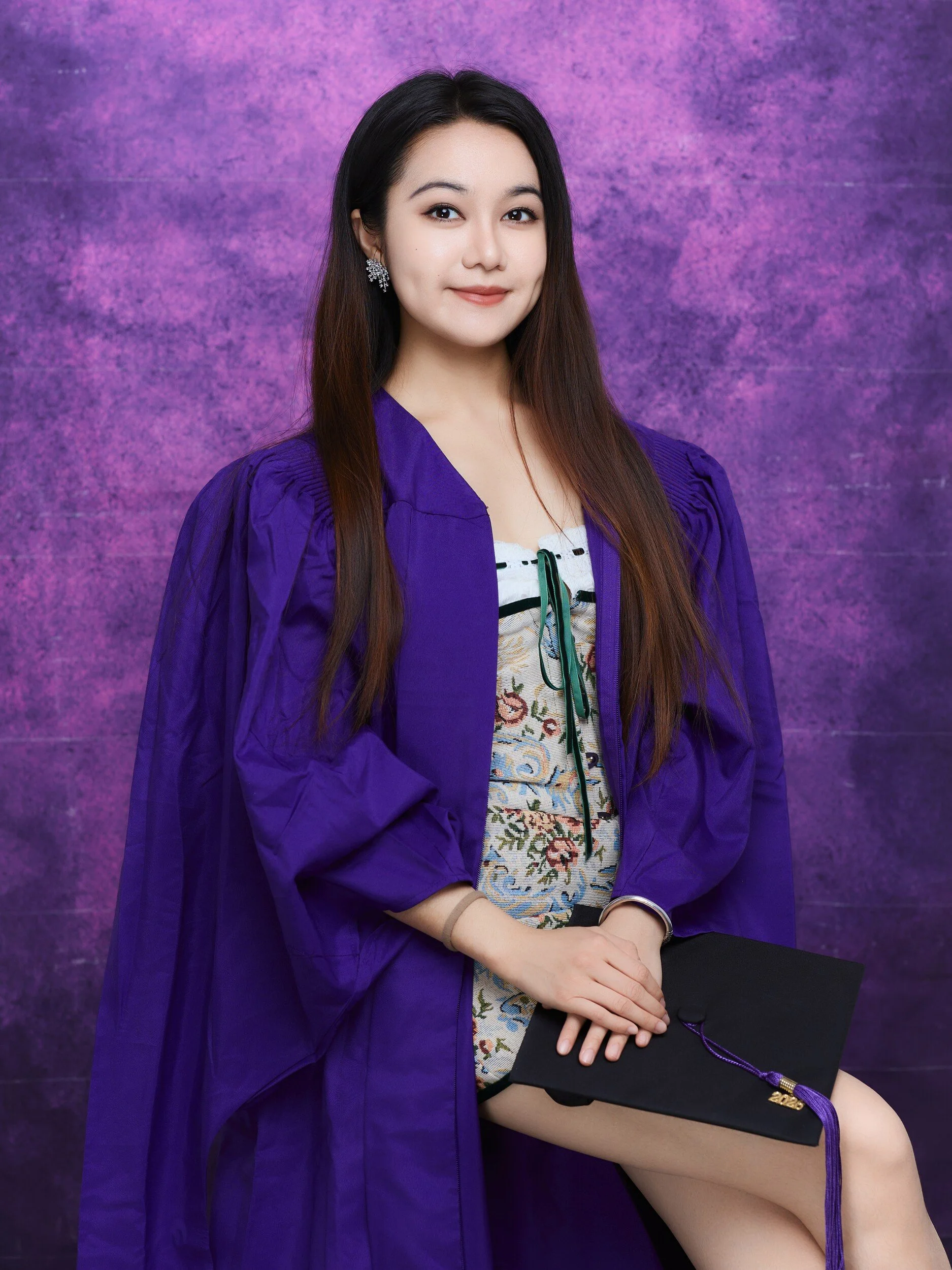 Seated NYU graduation portrait of a woman in a floral dress holding her cap