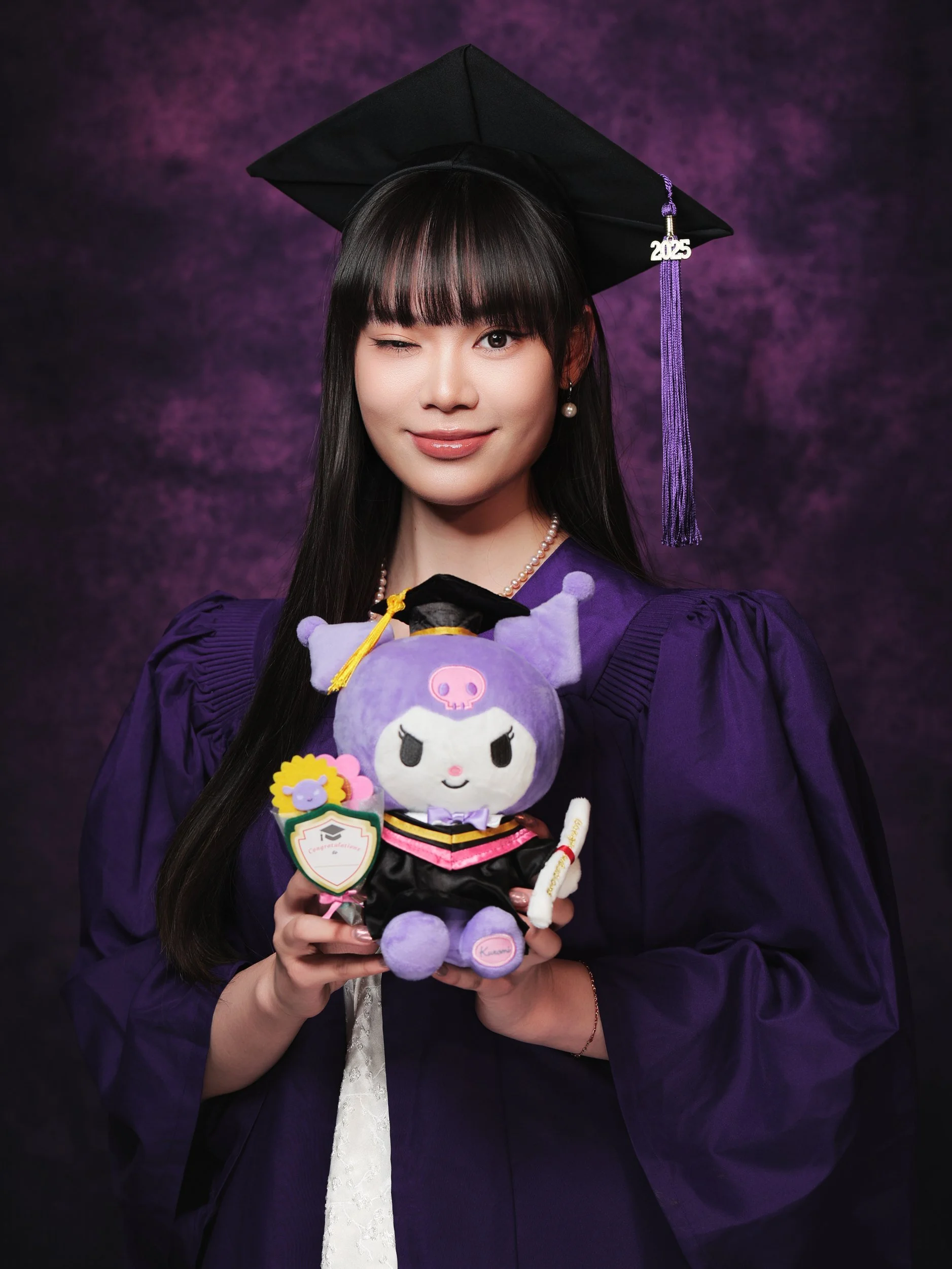 Graduation portrait of a woman in a purple gown holding a plush toy
