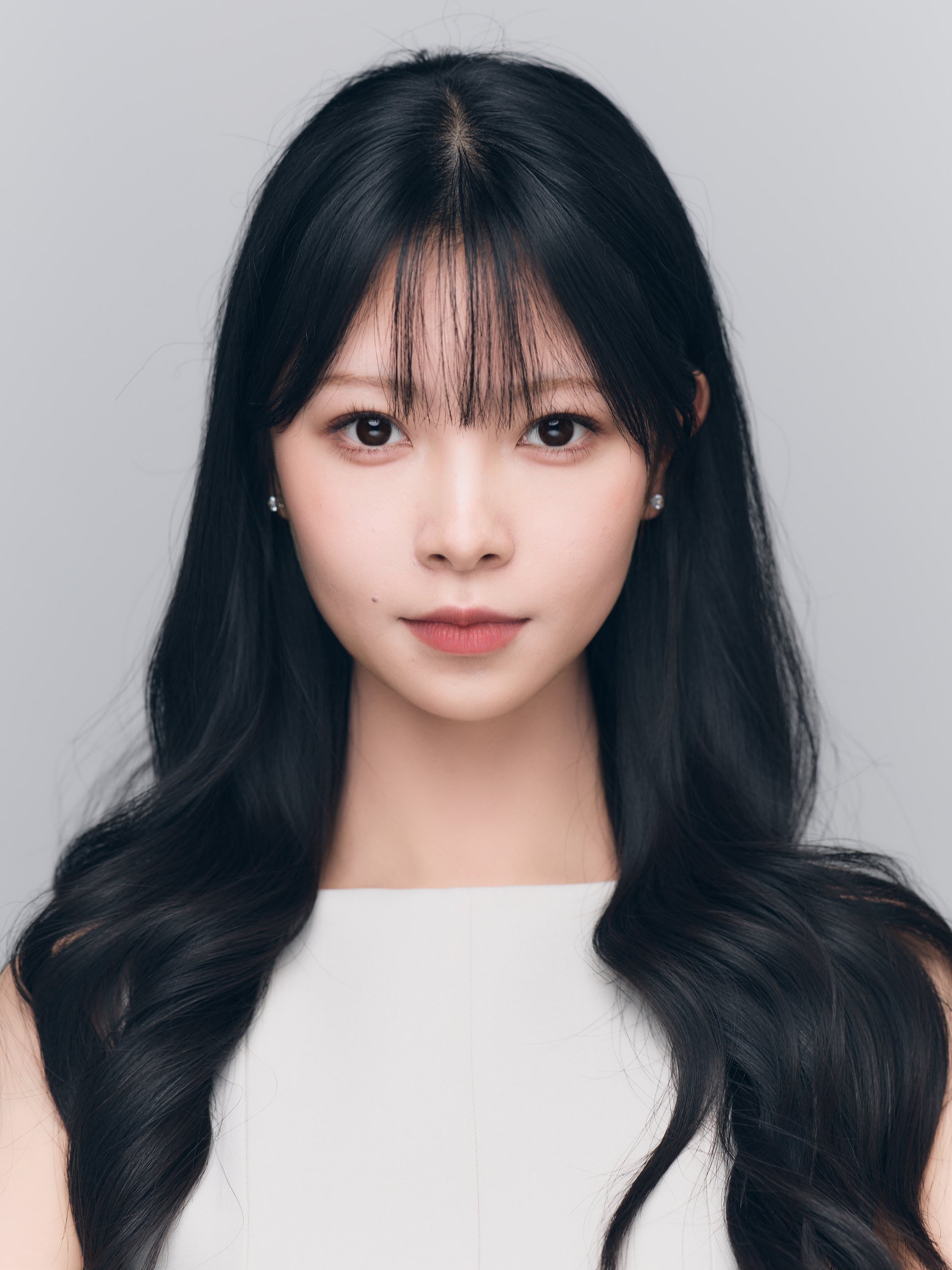 Front-facing ID-style headshot of a woman with long dark hair on light grey