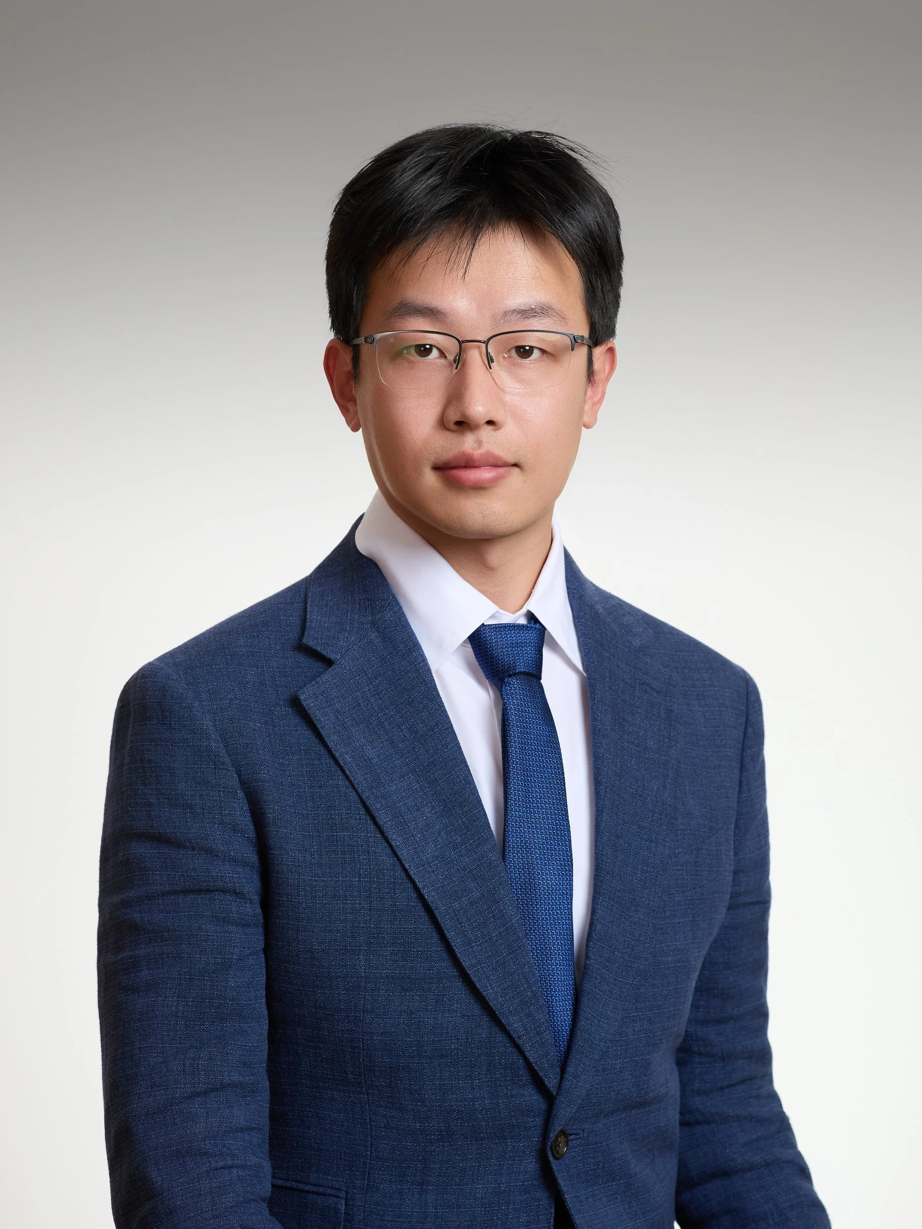 Corporate headshot of a man with glasses in a blue suit on a grey gradient