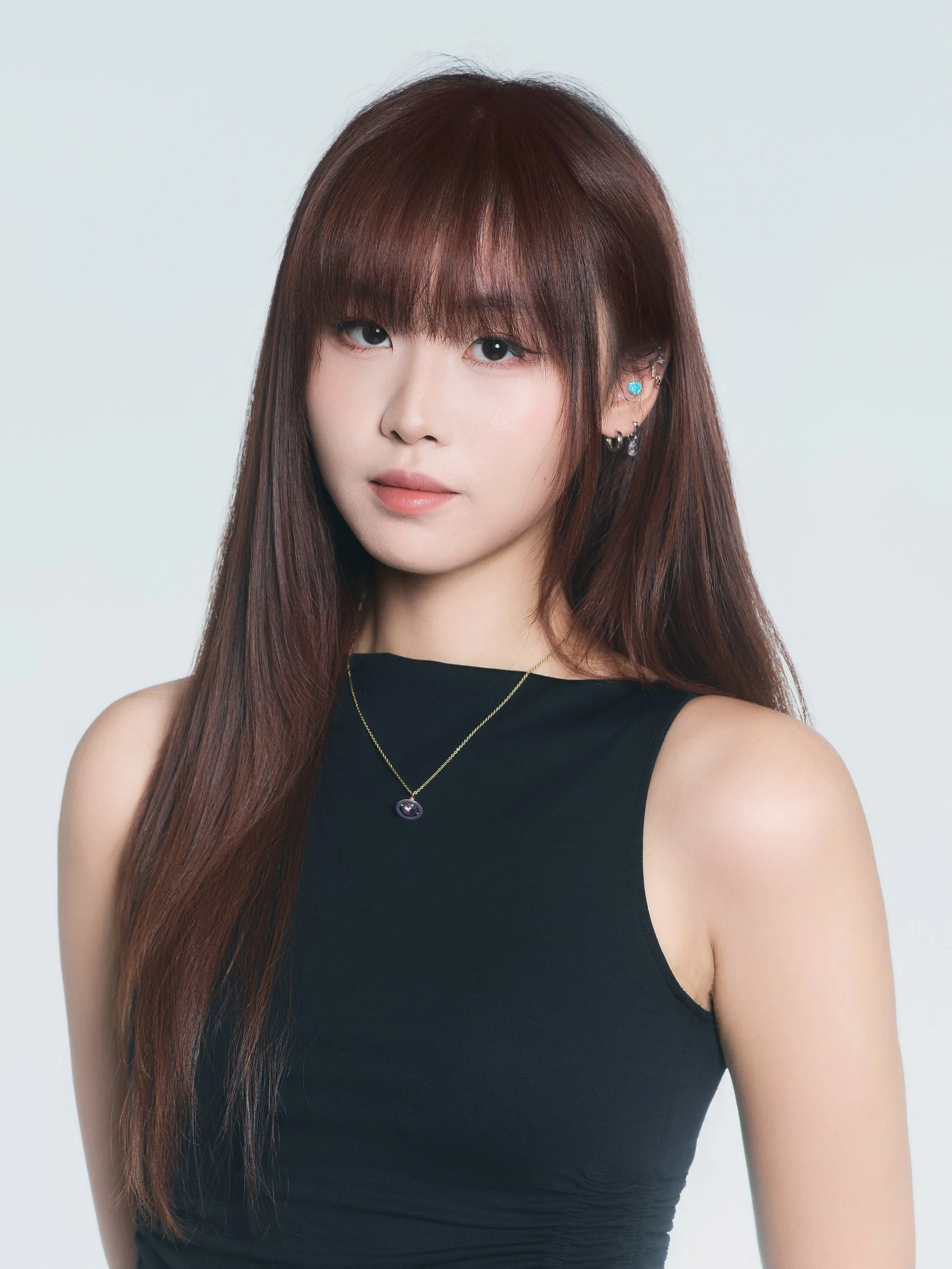 Headshot of a woman with bangs in a black sleeveless top on light grey