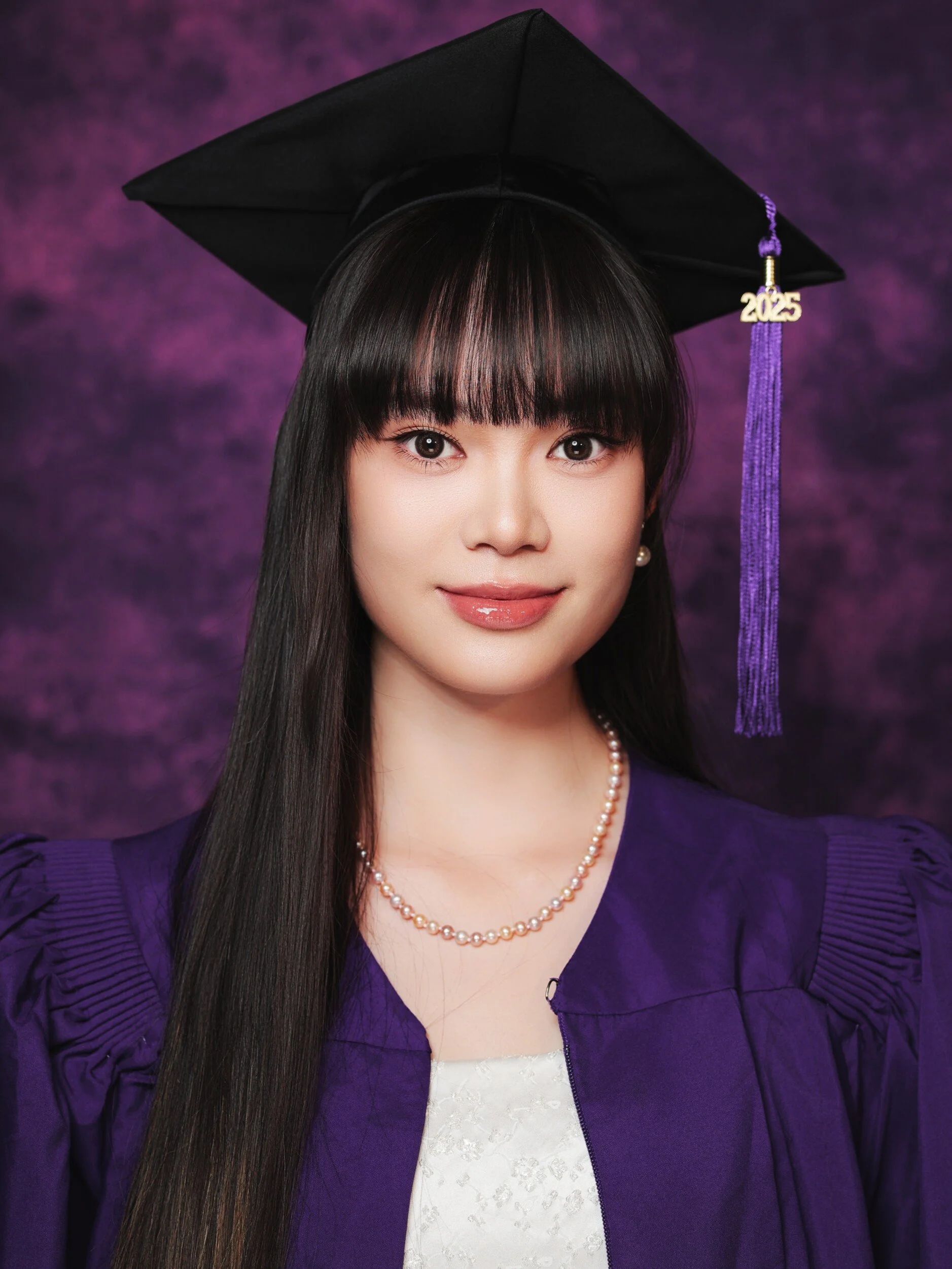 Close-up NYU graduation portrait of a woman with bangs and a pearl necklace