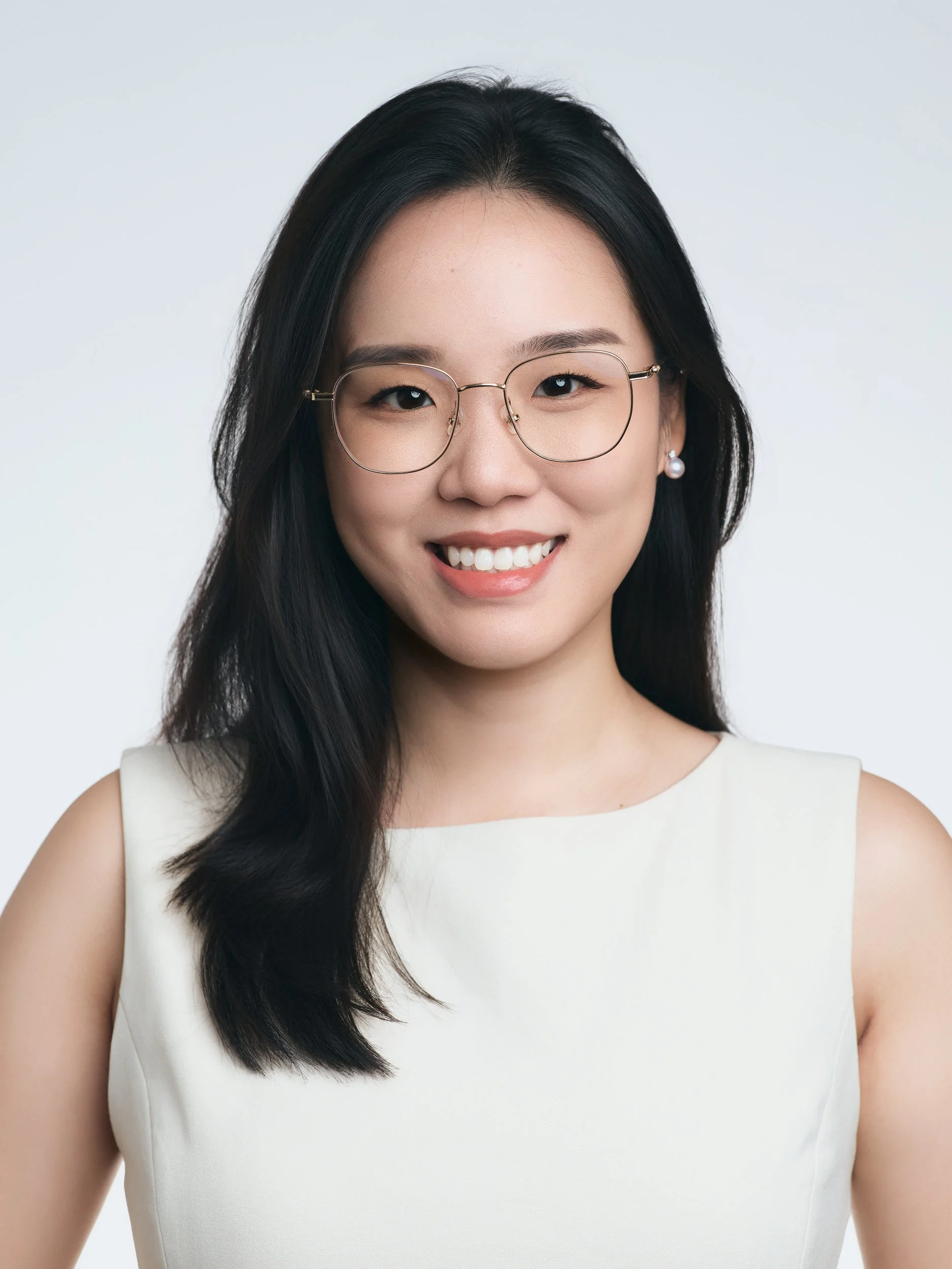 Professional headshot of a smiling woman with glasses in a white sleeveless top