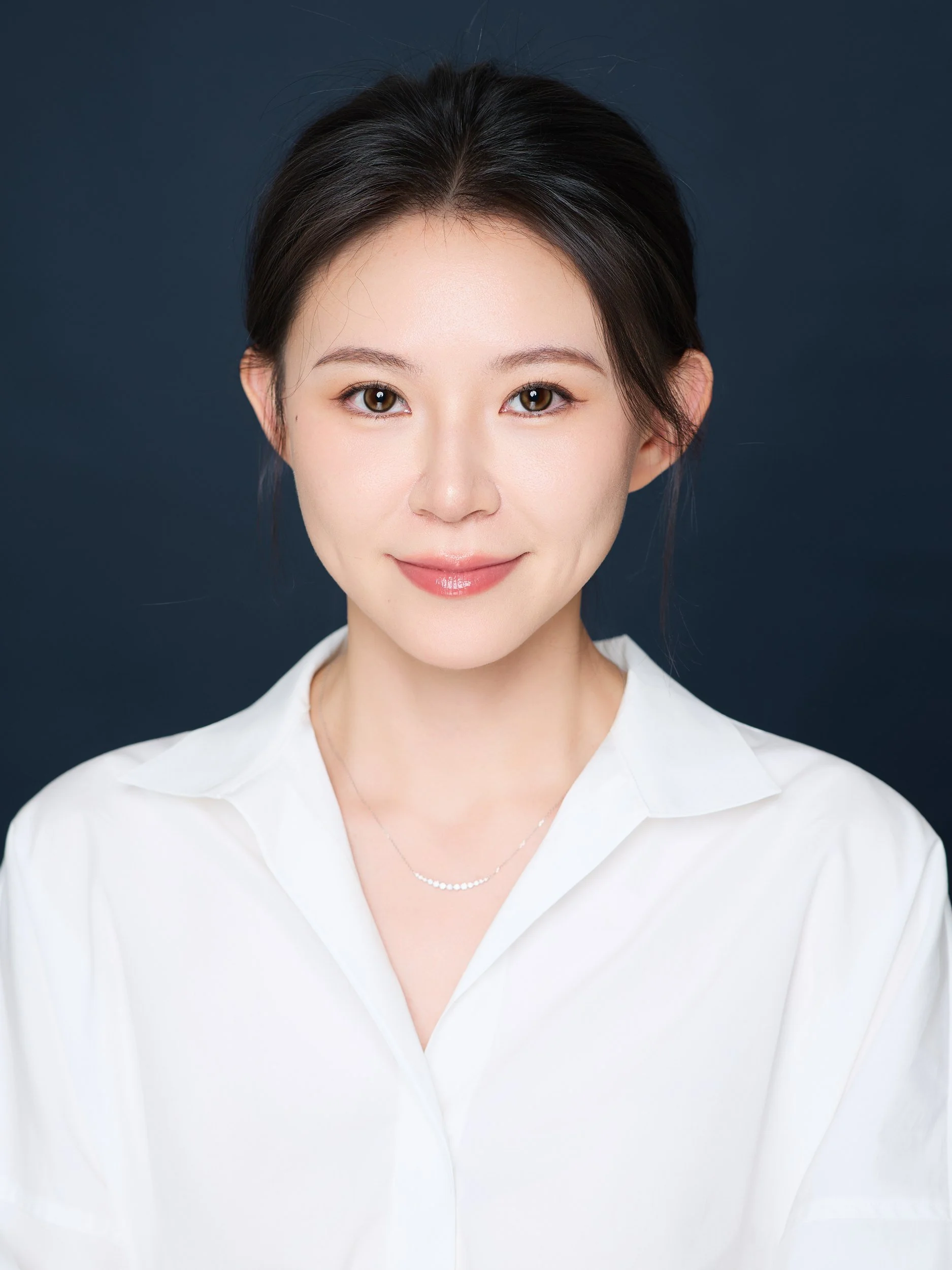 Professional headshot of a smiling woman in a white shirt on a navy backdrop