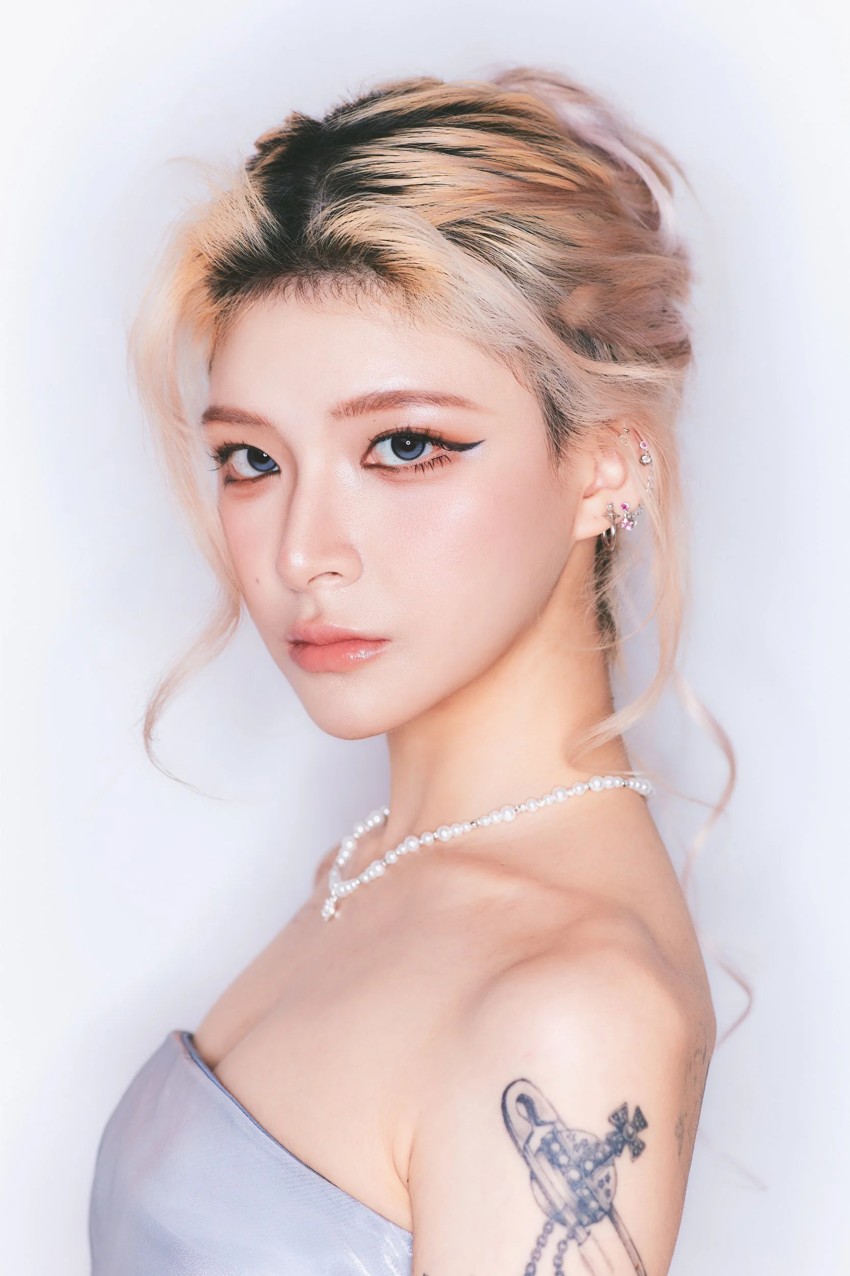 Profile portrait of a woman with a blonde updo and shoulder tattoo in a silver strapless top