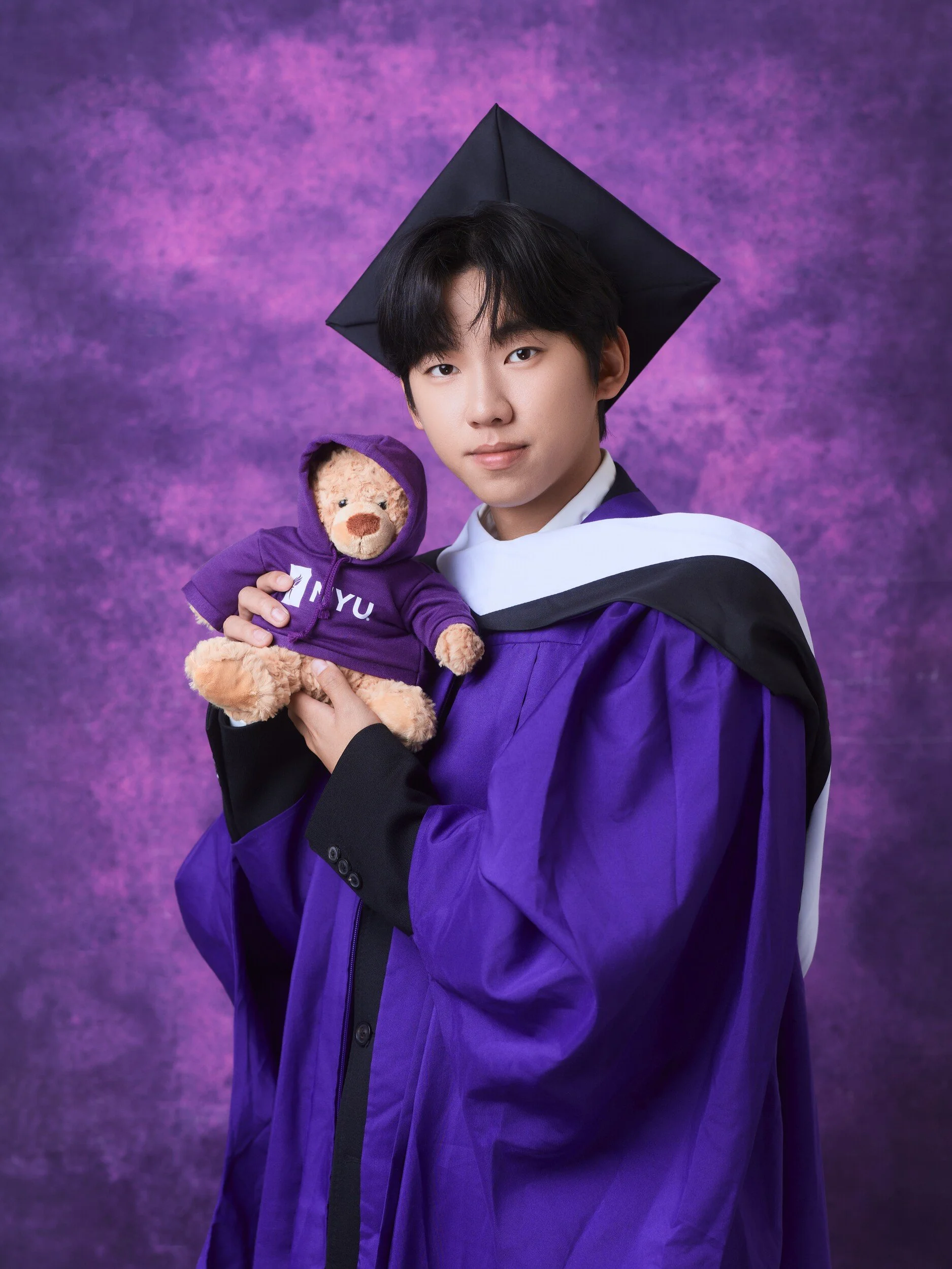 Graduate in cap holding an NYU teddy bear